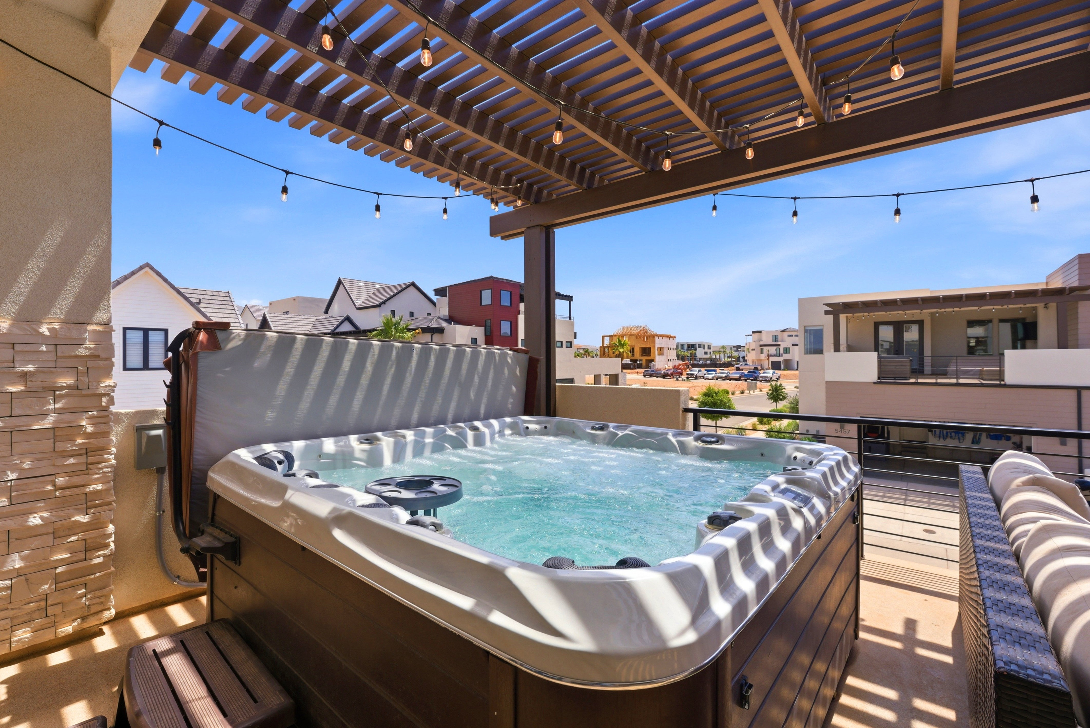 Rooftop patio featuring a built-in hot tub, pergola with string lights, and a stone-clad exterior wall