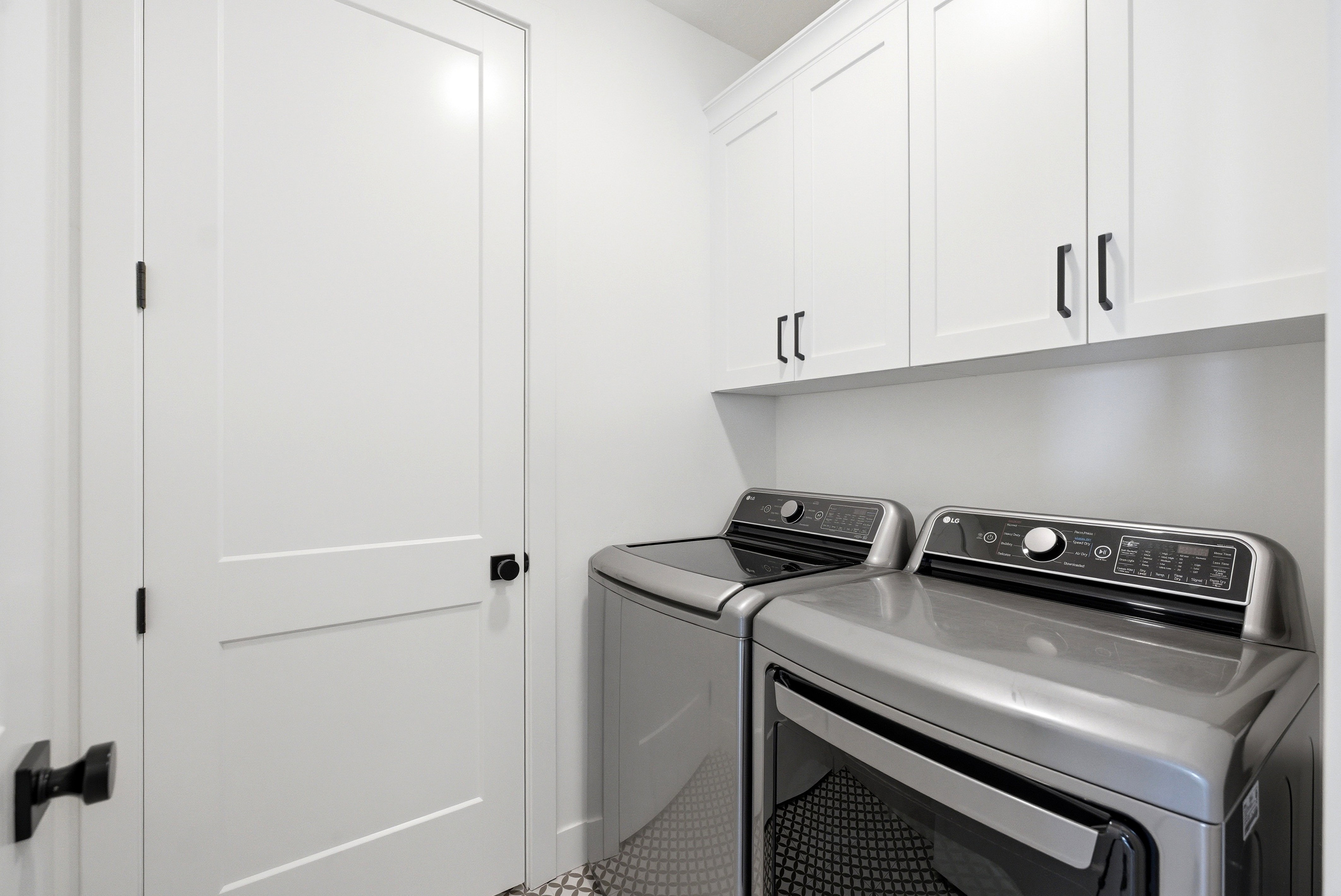 Dedicated laundry area featuring white shaker-style cabinetry with matte black hardware