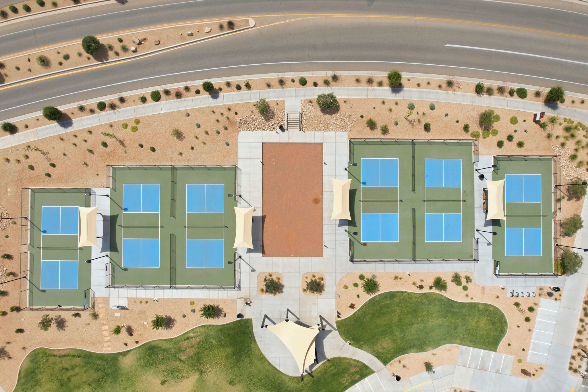 Outdoor recreation area featuring multiple courts, shaded seating, a central paved gathering space, and desert landscaping