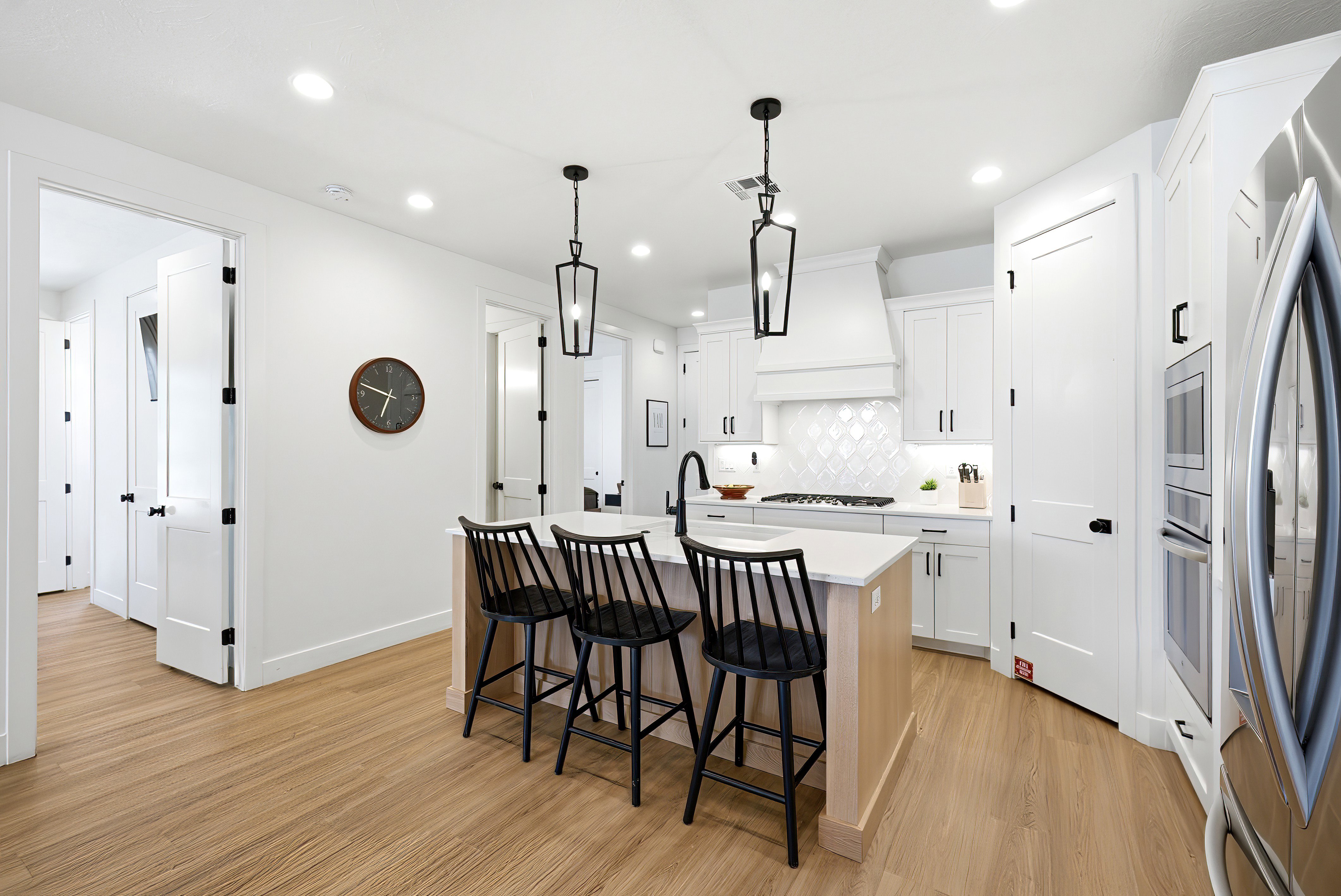 Contemporary kitchen featuring a light wood-finish island with seating for three, white cabinetry, integrated stainless steel appliances, and a diagonal patterned tile backsplash