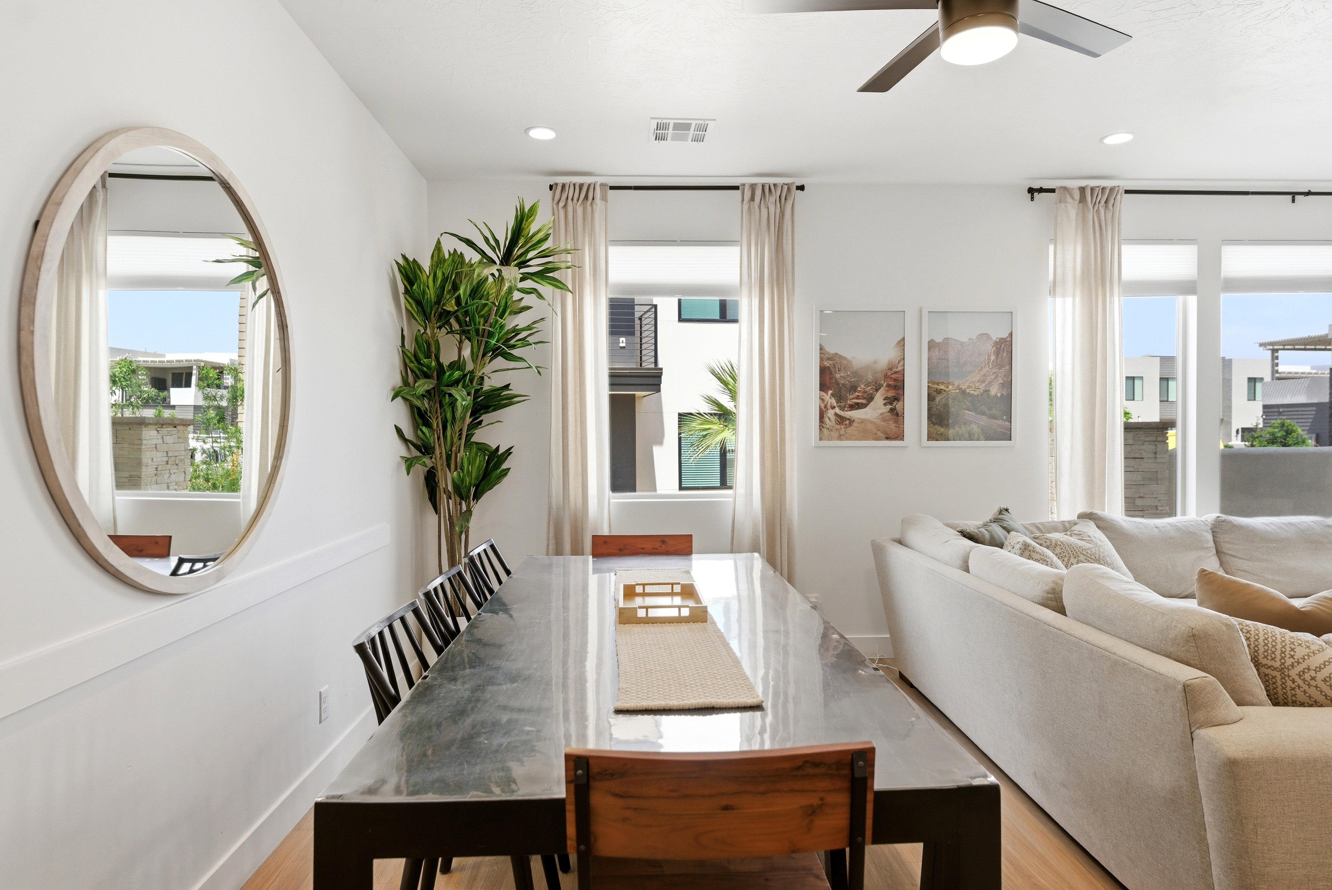 Open-concept living space with light wood-finish flooring, a contemporary ceiling fan, recessed lighting, and large windows with privacy drapes