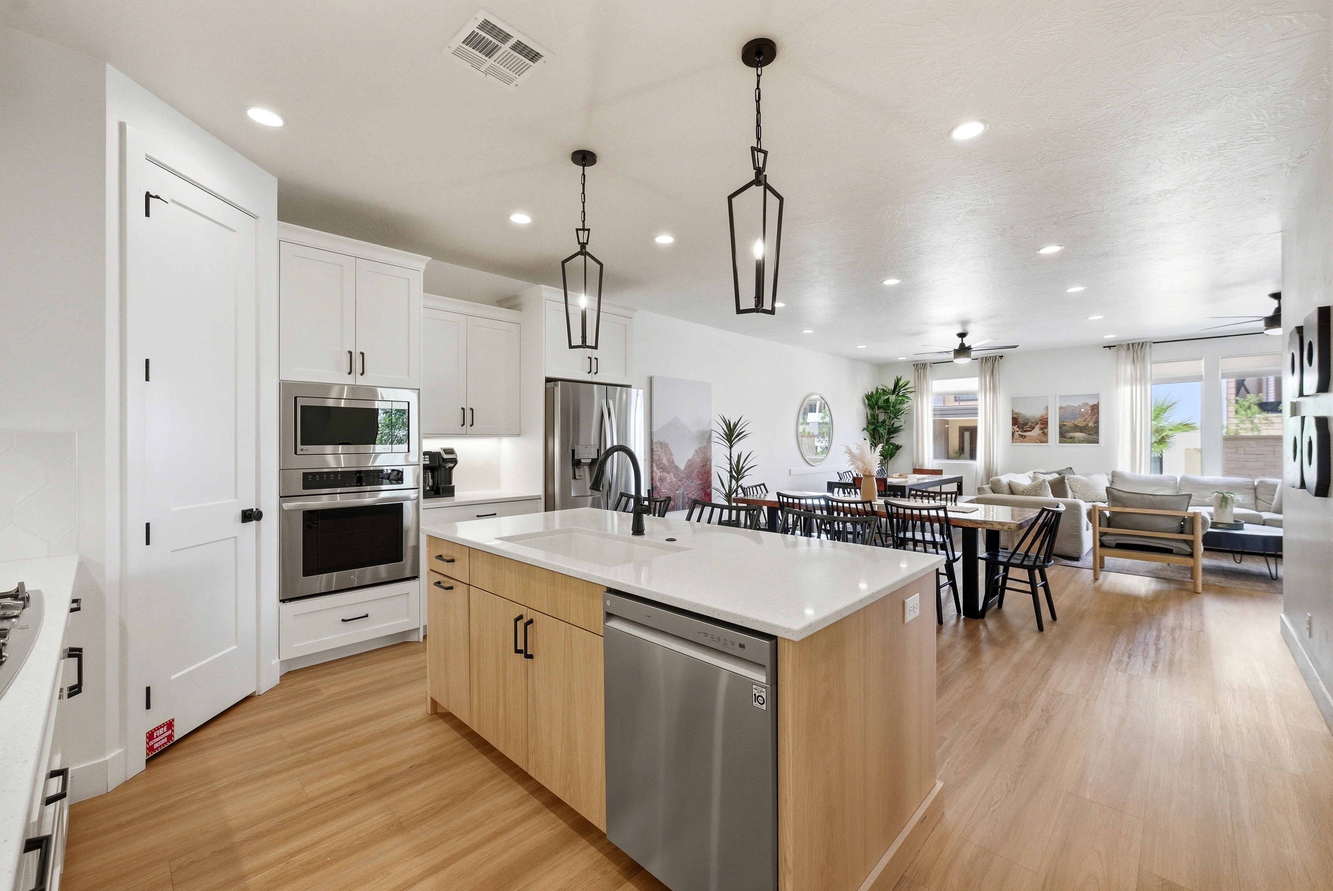 Open-concept kitchen featuring an island with a white countertop, light wood-finish cabinetry, stainless steel appliances, and wood-finish flooring