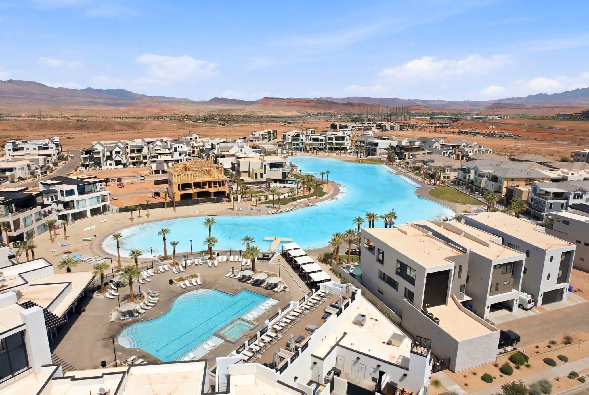 Expansive aerial view of a community featuring a large, bright blue lagoon with sandy edges, surrounded by multiple residential structures