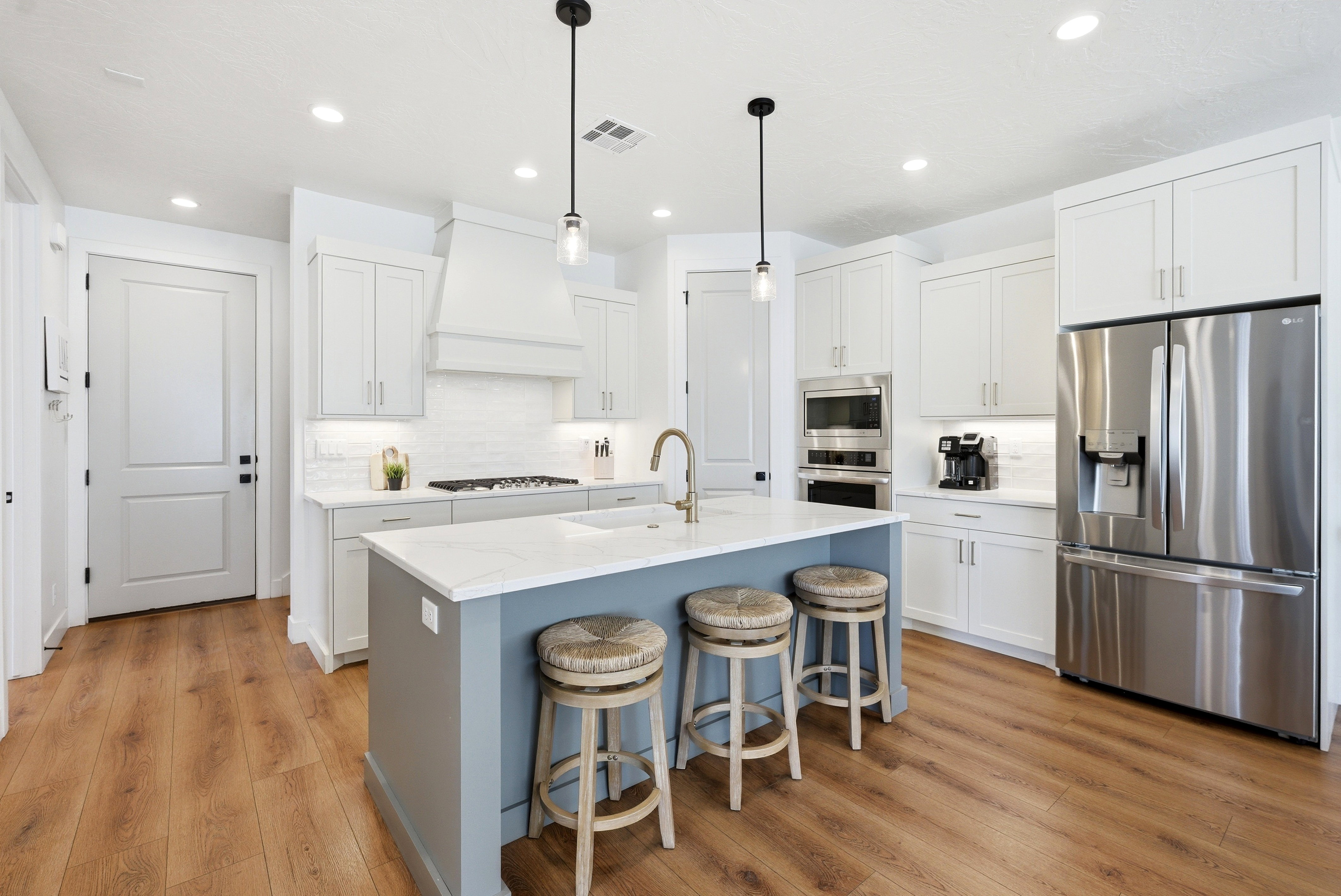 Gourmet kitchen featuring a central island with countertop seating, white shaker-style cabinetry, stainless steel appliances, wood-finish flooring, and recessed lighting
