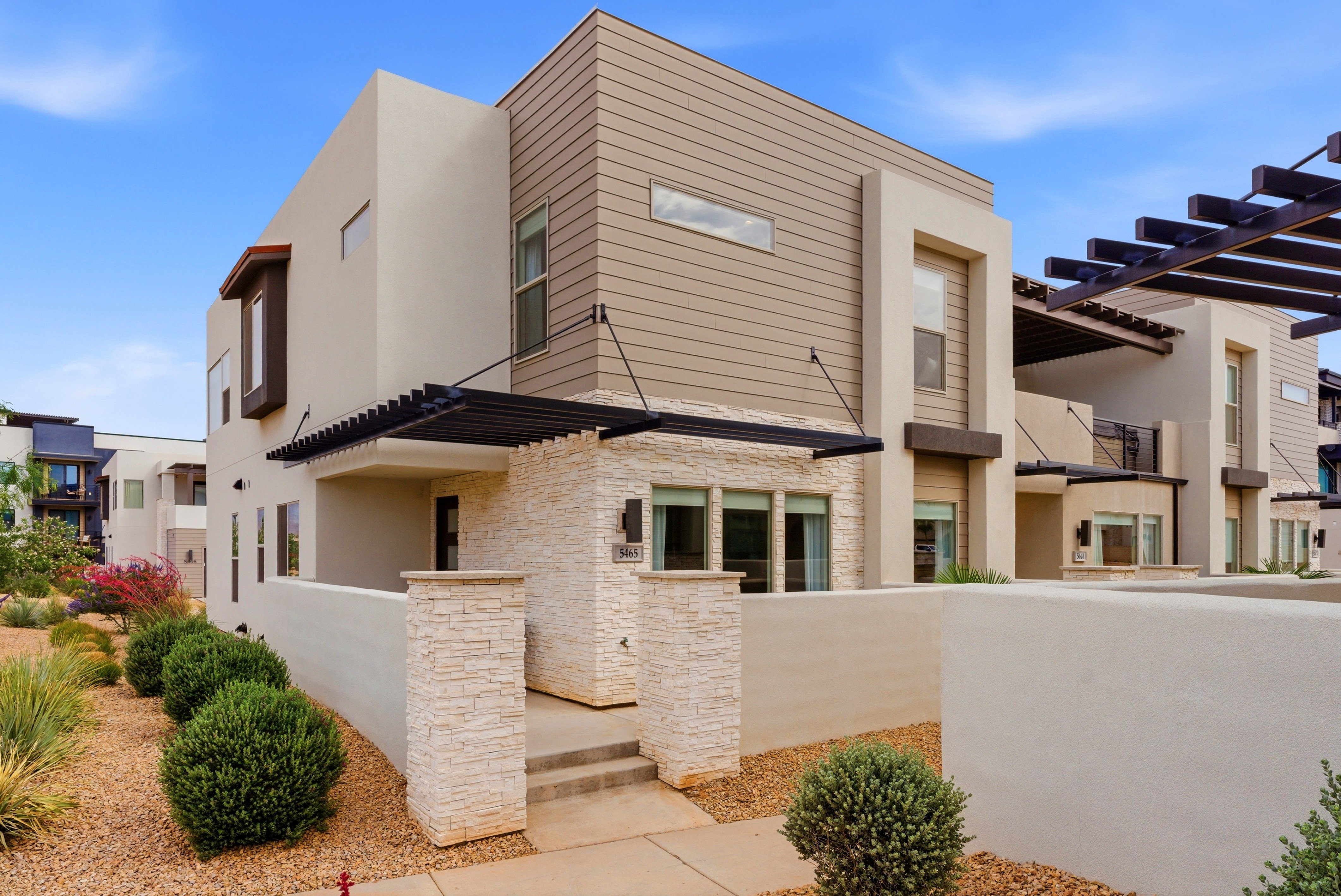 Contemporary multi-level residence featuring stucco and horizontal siding, stone veneer accents, and an architectural pergola over the entry