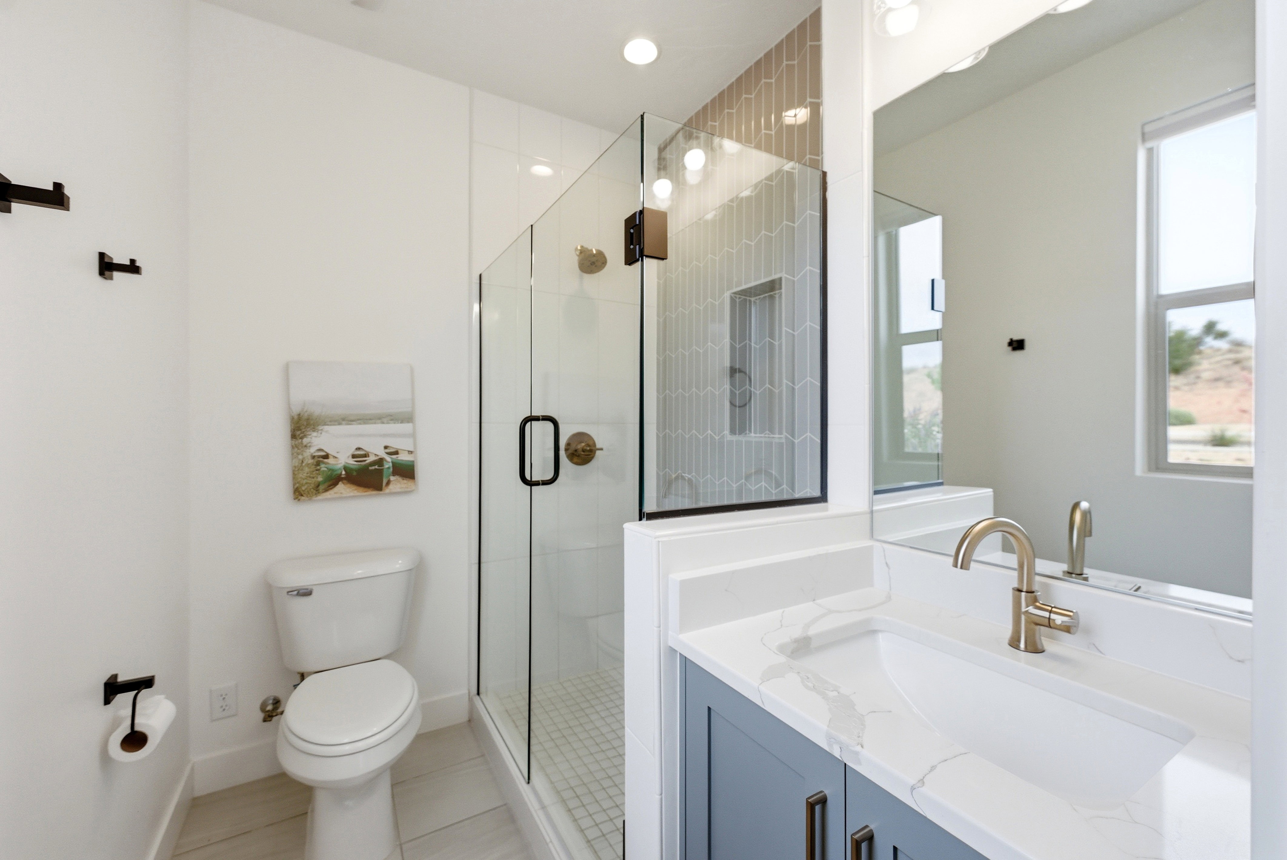 Bathroom featuring a frameless glass shower enclosure with hex tile surround and built-in niche, a single vanity with a quartz countertop, integrated sink, and brushed brass faucet, and wood-finish flooring