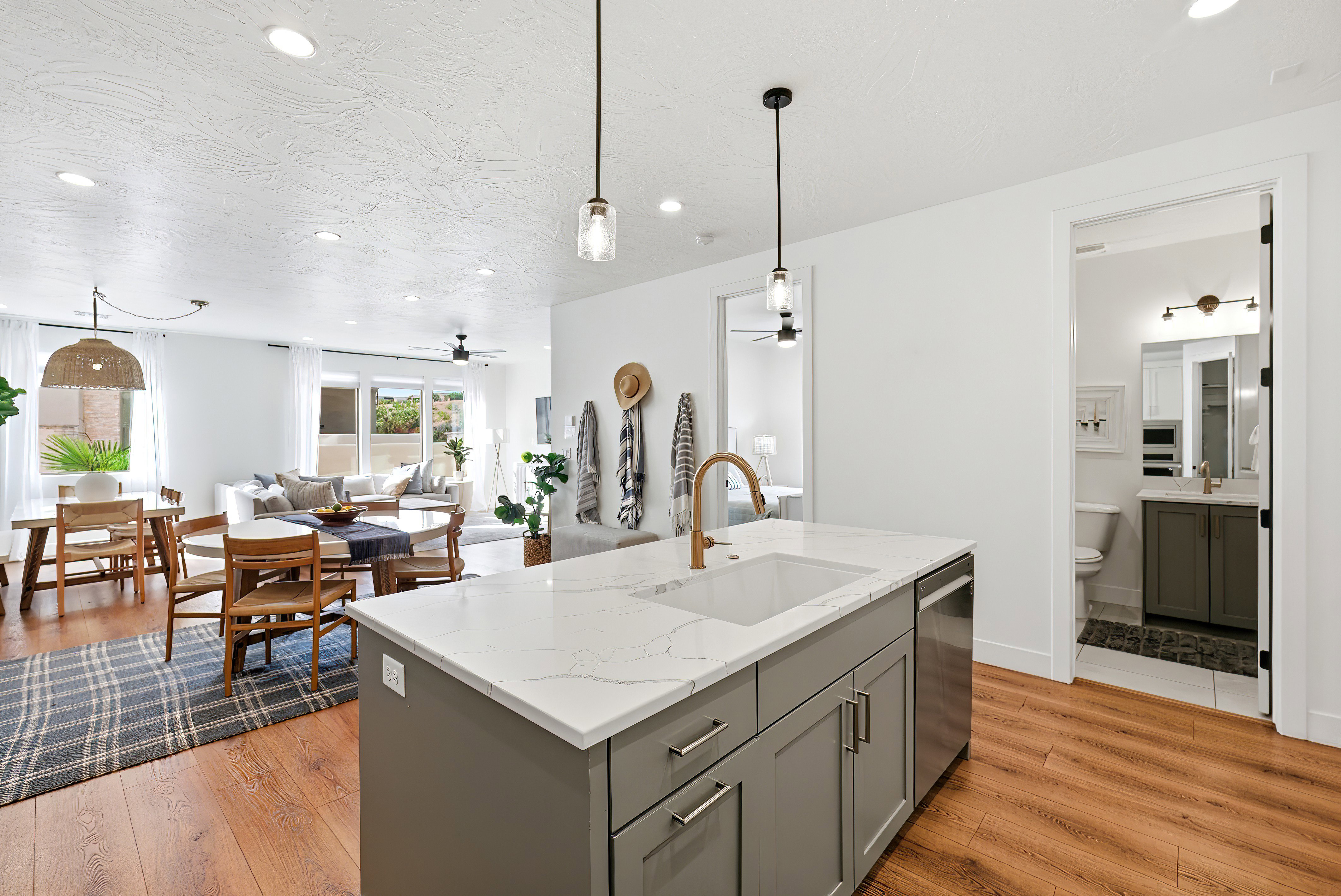 Open-concept living area featuring wood-finish flooring, recessed lighting, and a kitchen island with a white countertop and integrated sink