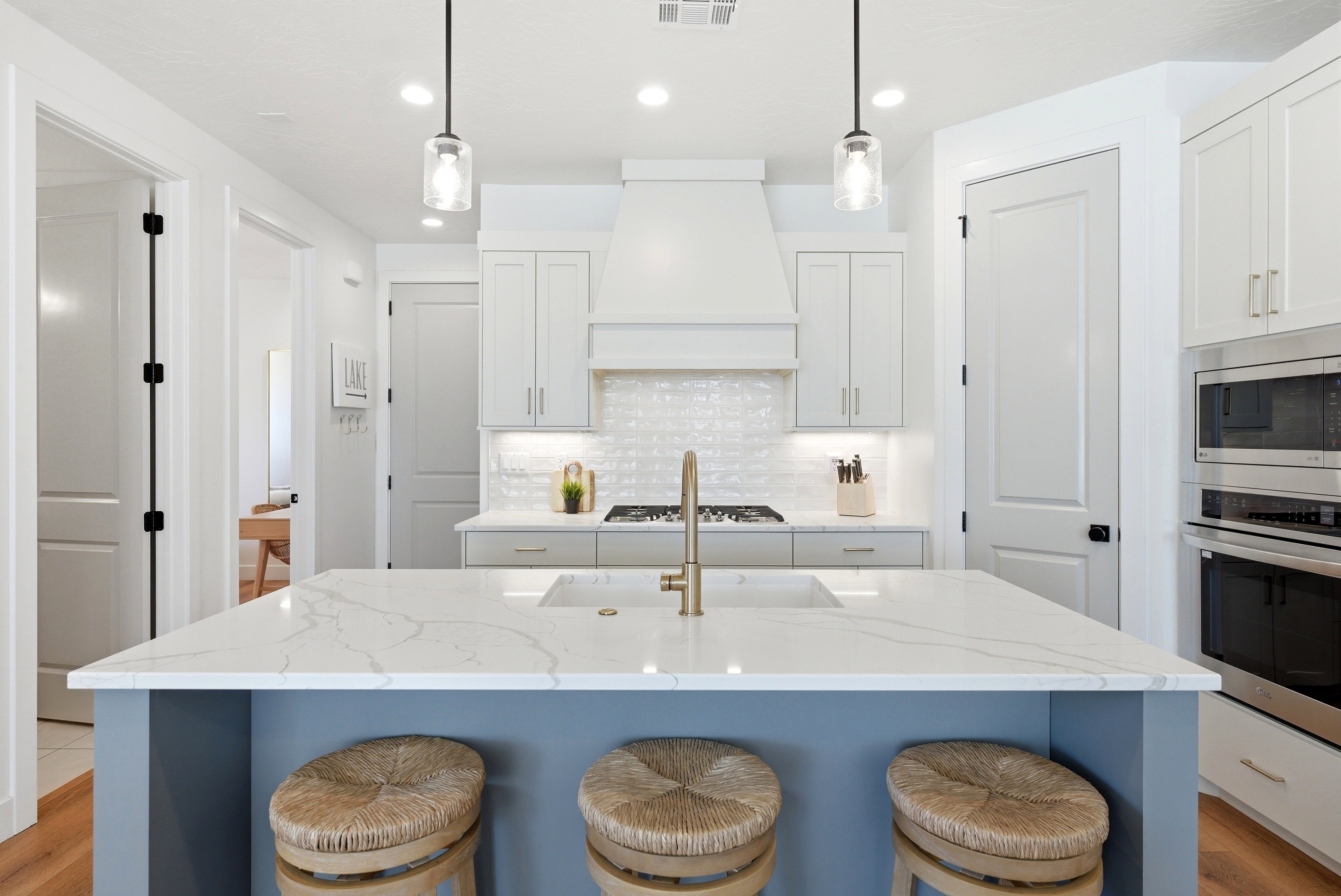 Contemporary kitchen featuring a large central island with a light-toned countertop and blue base cabinetry, white shaker-style perimeter cabinets, stainless steel appliances including a built-in microwave and oven, a white tile backsplash, and recessed l