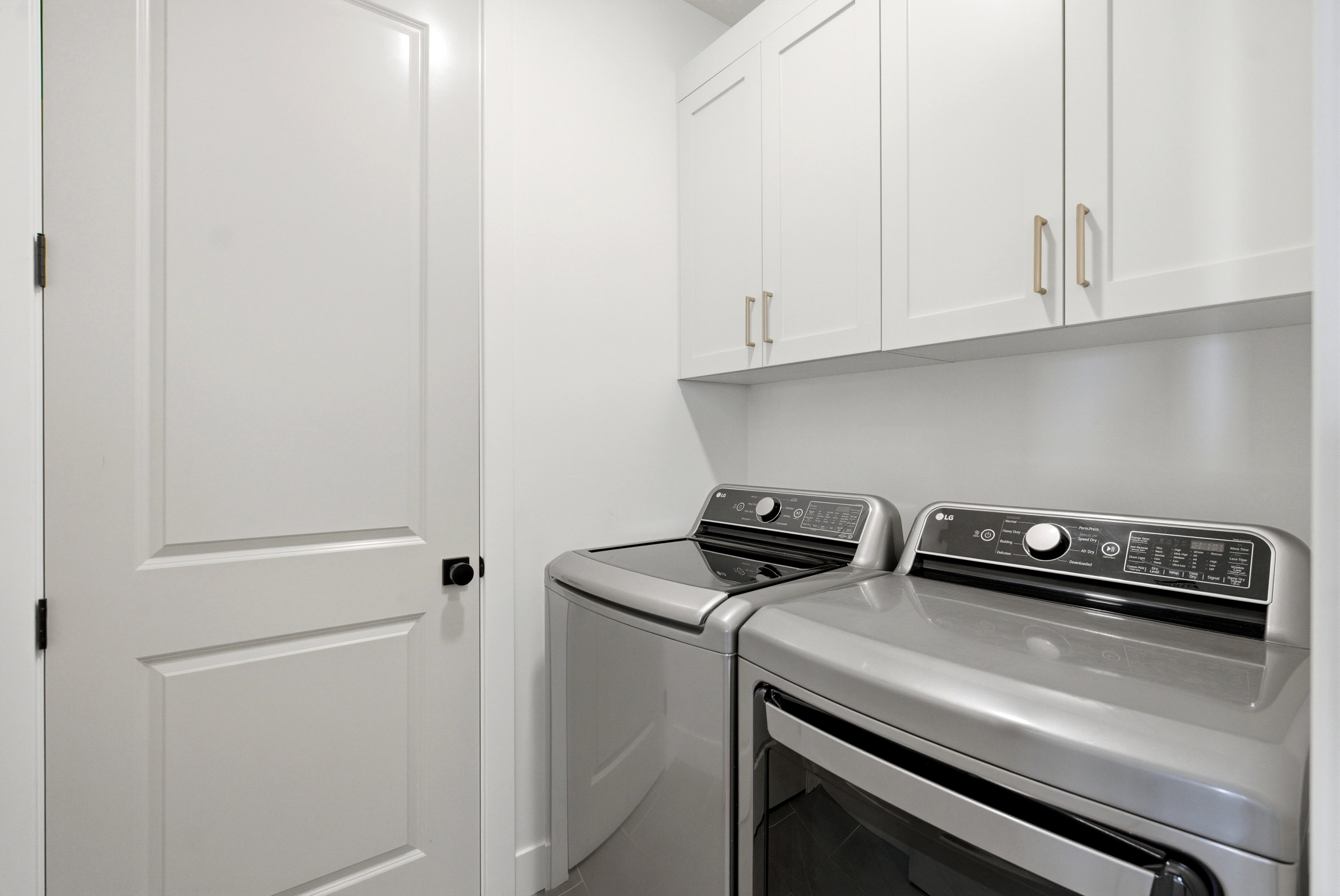 Dedicated laundry area featuring white shaker-style cabinetry with gold-tone hardware, providing overhead storage