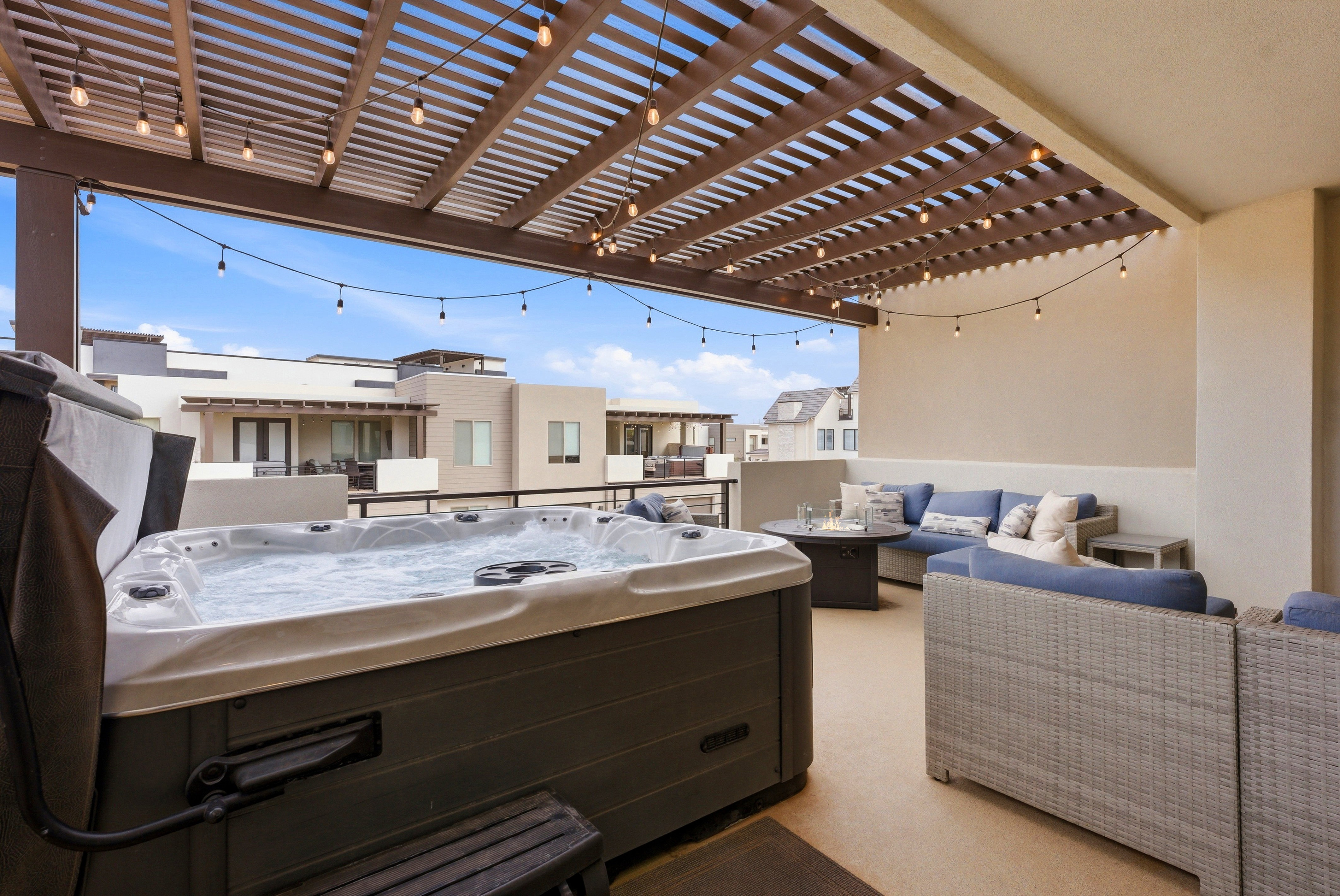 Spacious rooftop patio featuring a built-in hot tub, slatted pergola, string lighting, and an open sky