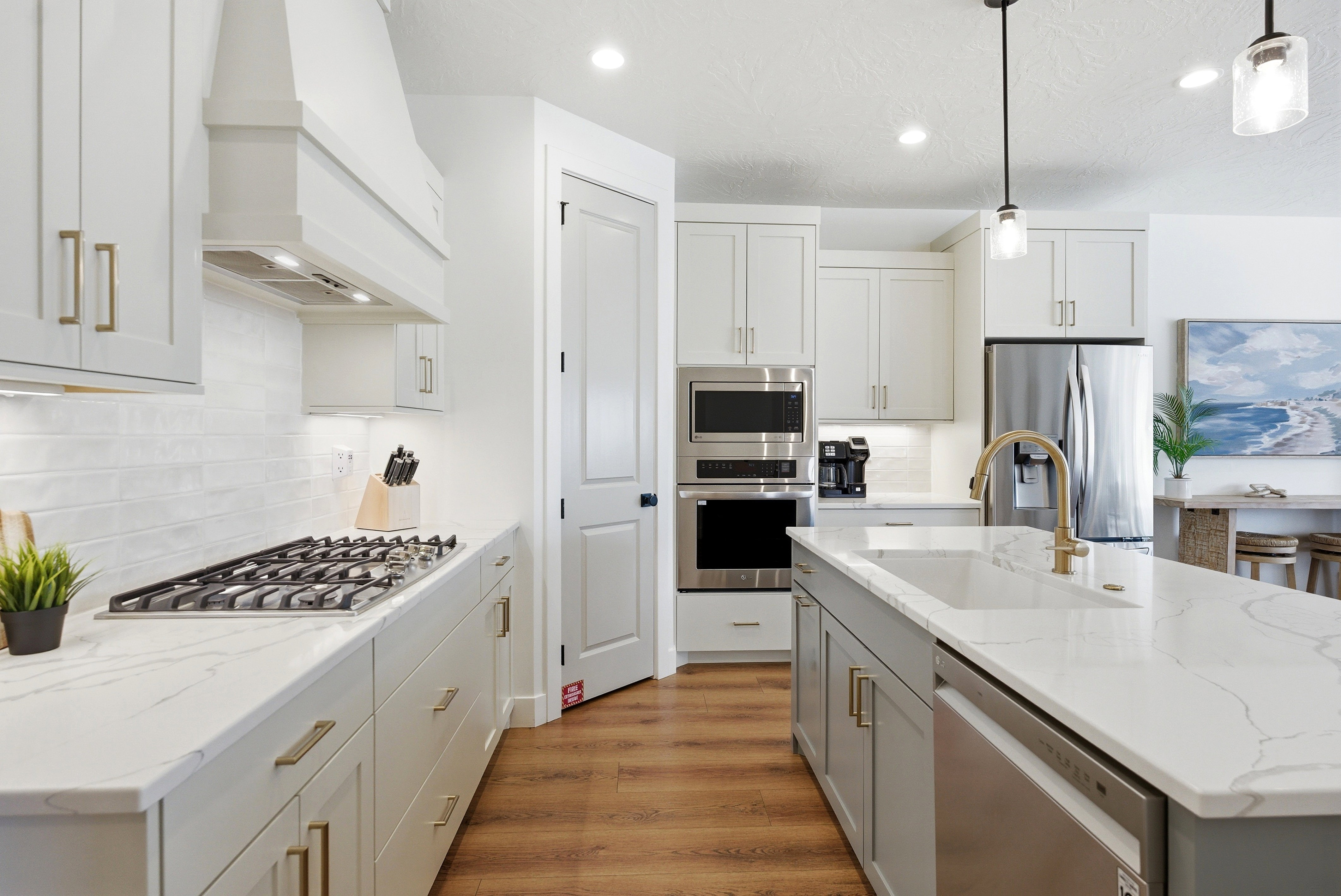 Kitchen featuring light-finish cabinetry, stainless steel appliances, a center island with sink, wood-finish flooring, and light-tone countertops