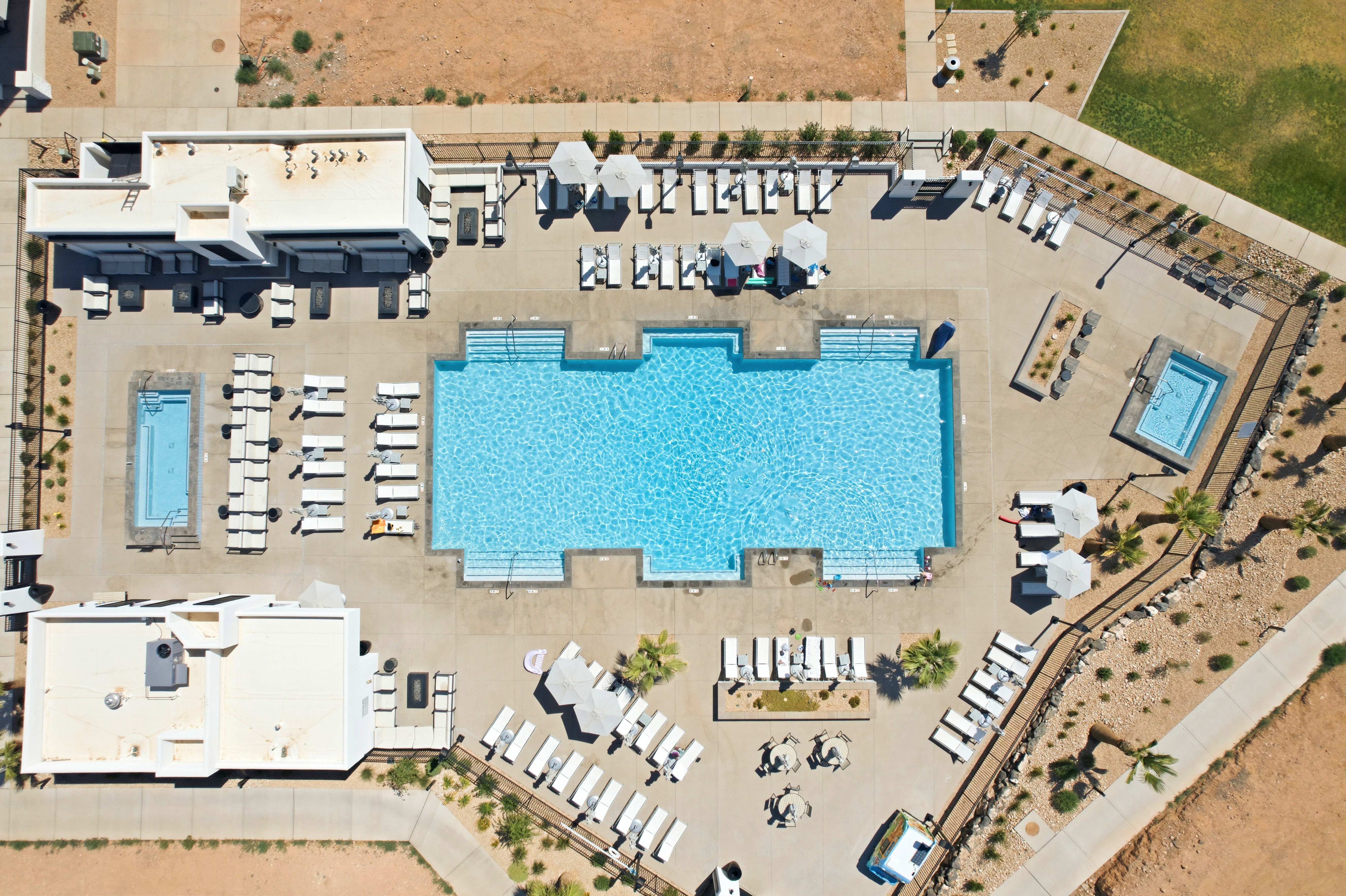 Expansive aquatic amenity featuring a large main swimming pool, two additional smaller pools, surrounding paver decking, and multiple lounge areas with umbrellas
