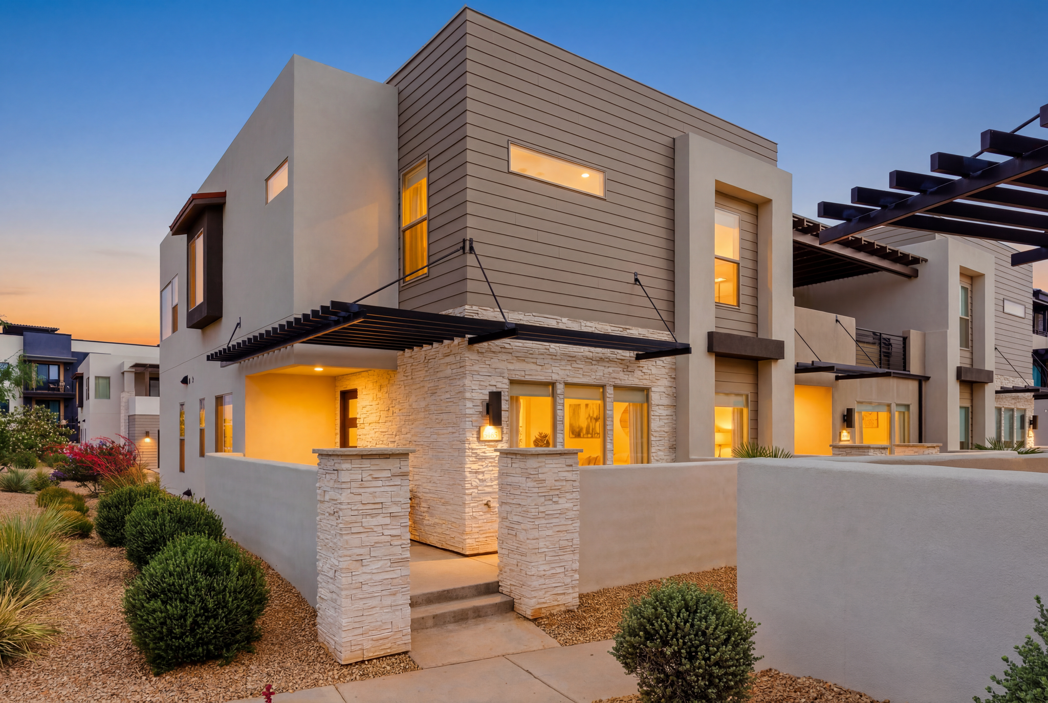 Modern multi-level residence featuring stucco and horizontal siding, stone veneer accents, an entry pergola, and integrated outdoor lighting