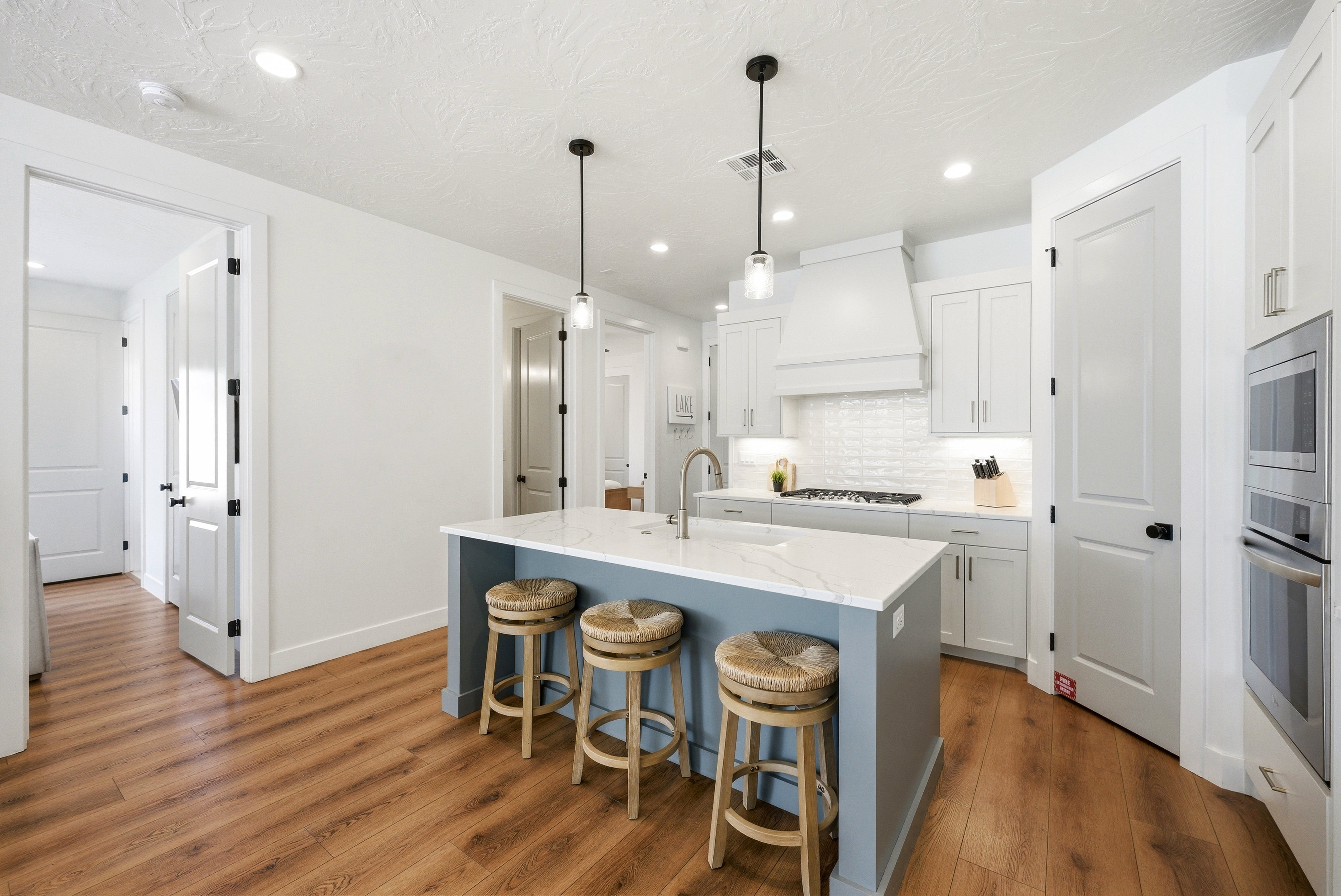 Kitchen featuring a central island with a light-toned countertop, pendant lighting, wood-finish flooring, white cabinetry, and stainless steel built-in appliances