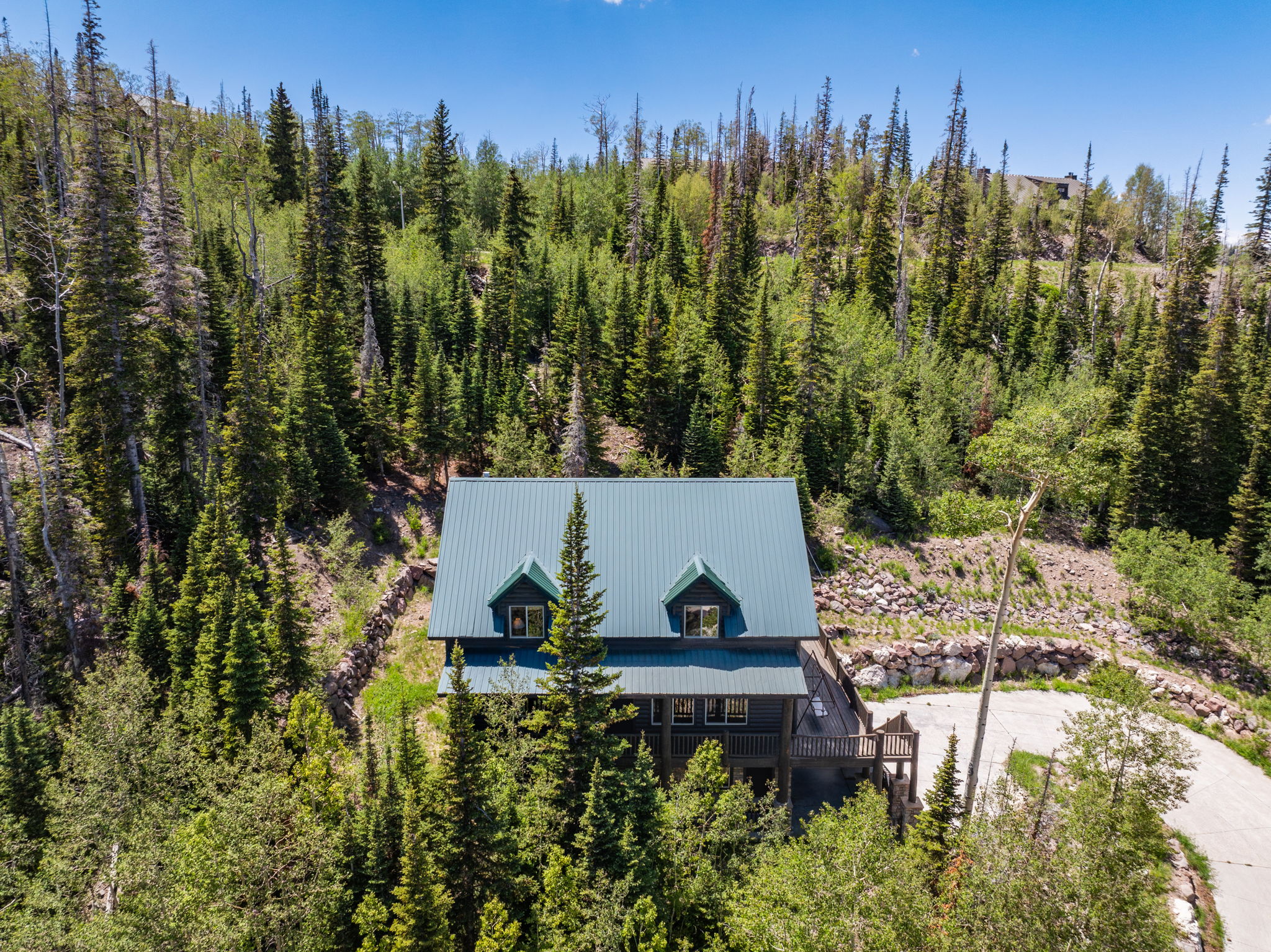 Mountain property featuring a dark-toned exterior with a blue metal roof, multiple dormer windows, and a wraparound deck