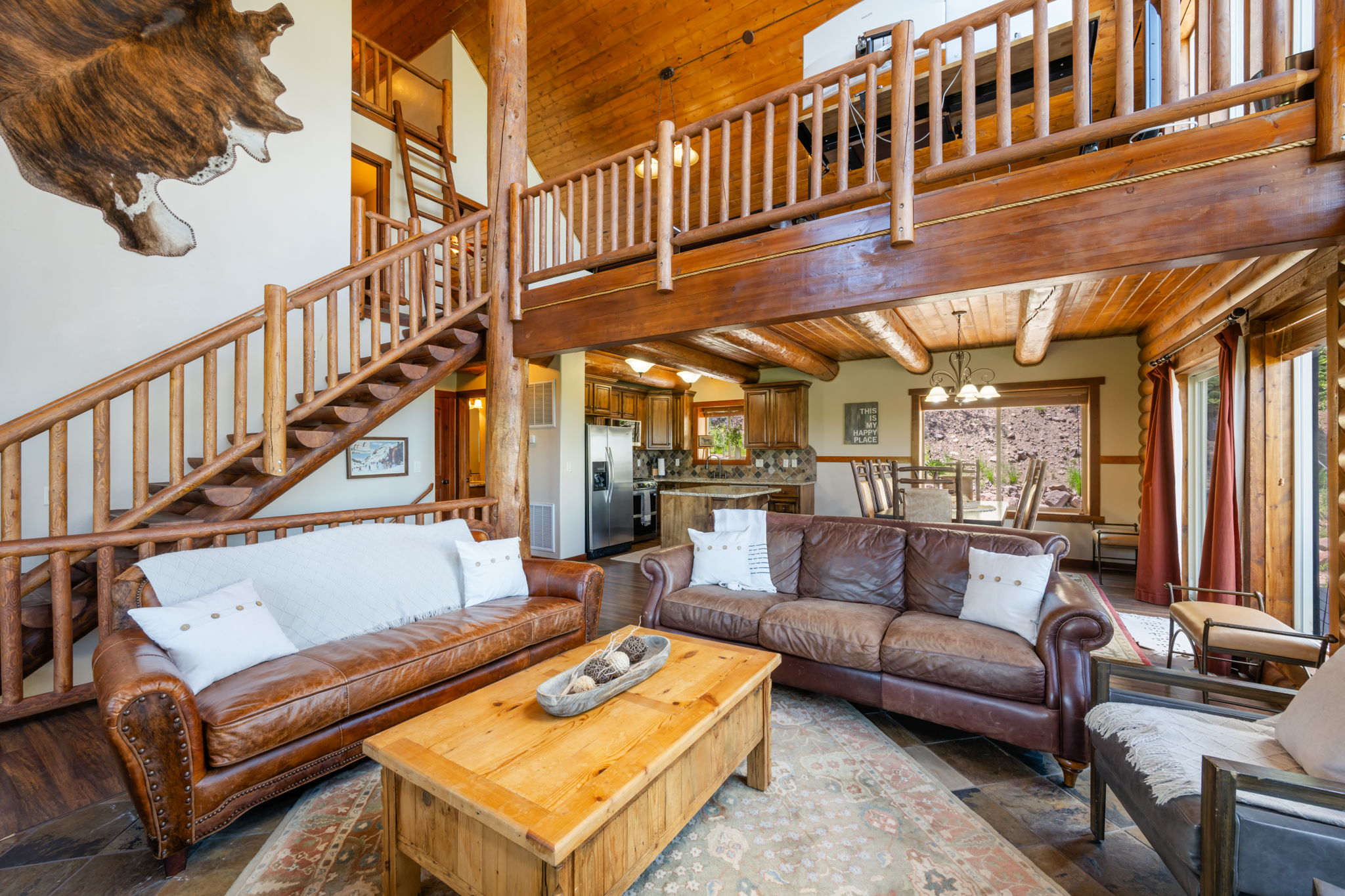 Two-story great room featuring a grand timber staircase, exposed wood beams, wood-finish flooring, and a second-story loft