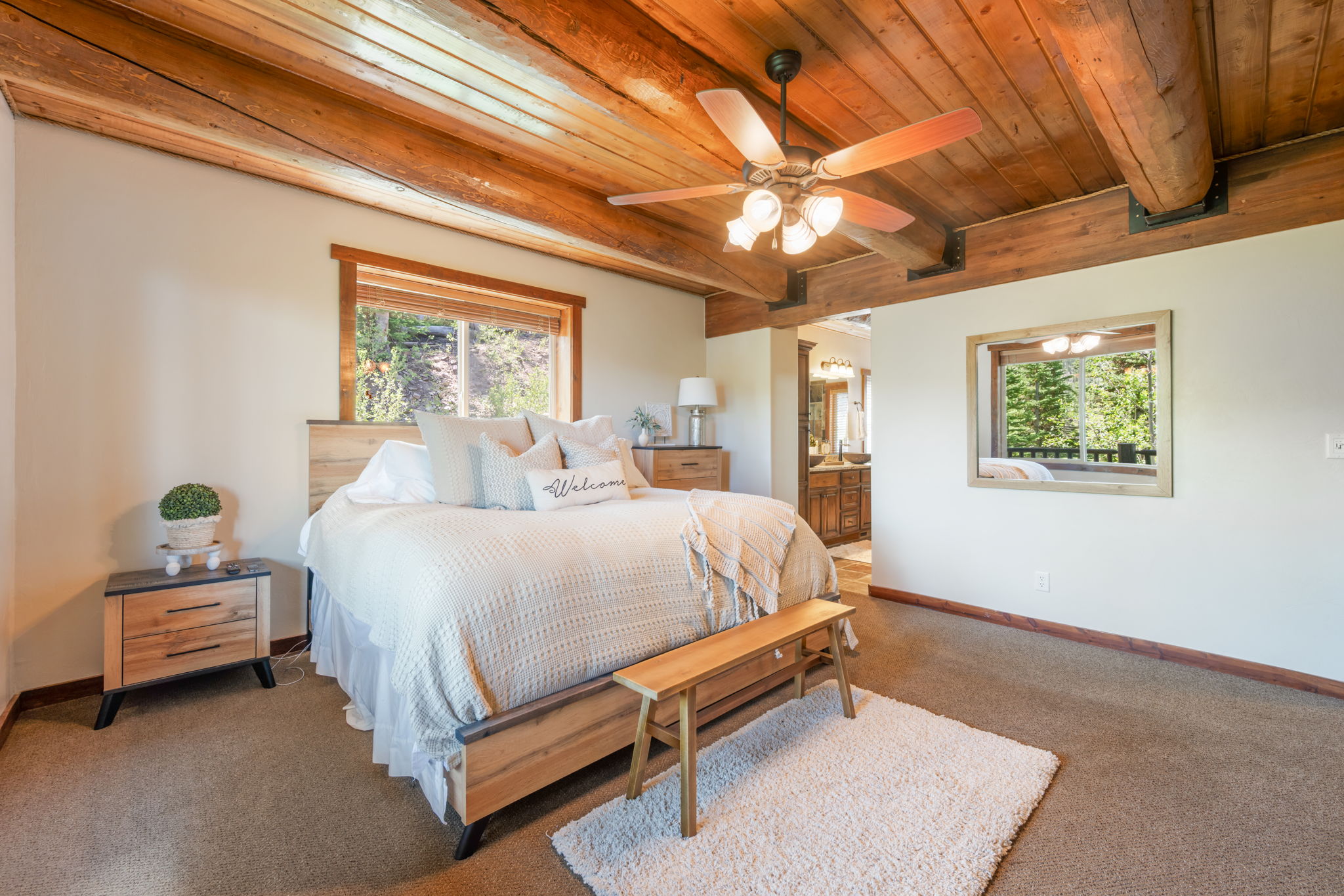 Bedroom featuring exposed log beam ceiling, wood-frame window, and a ceiling fan with integrated lighting