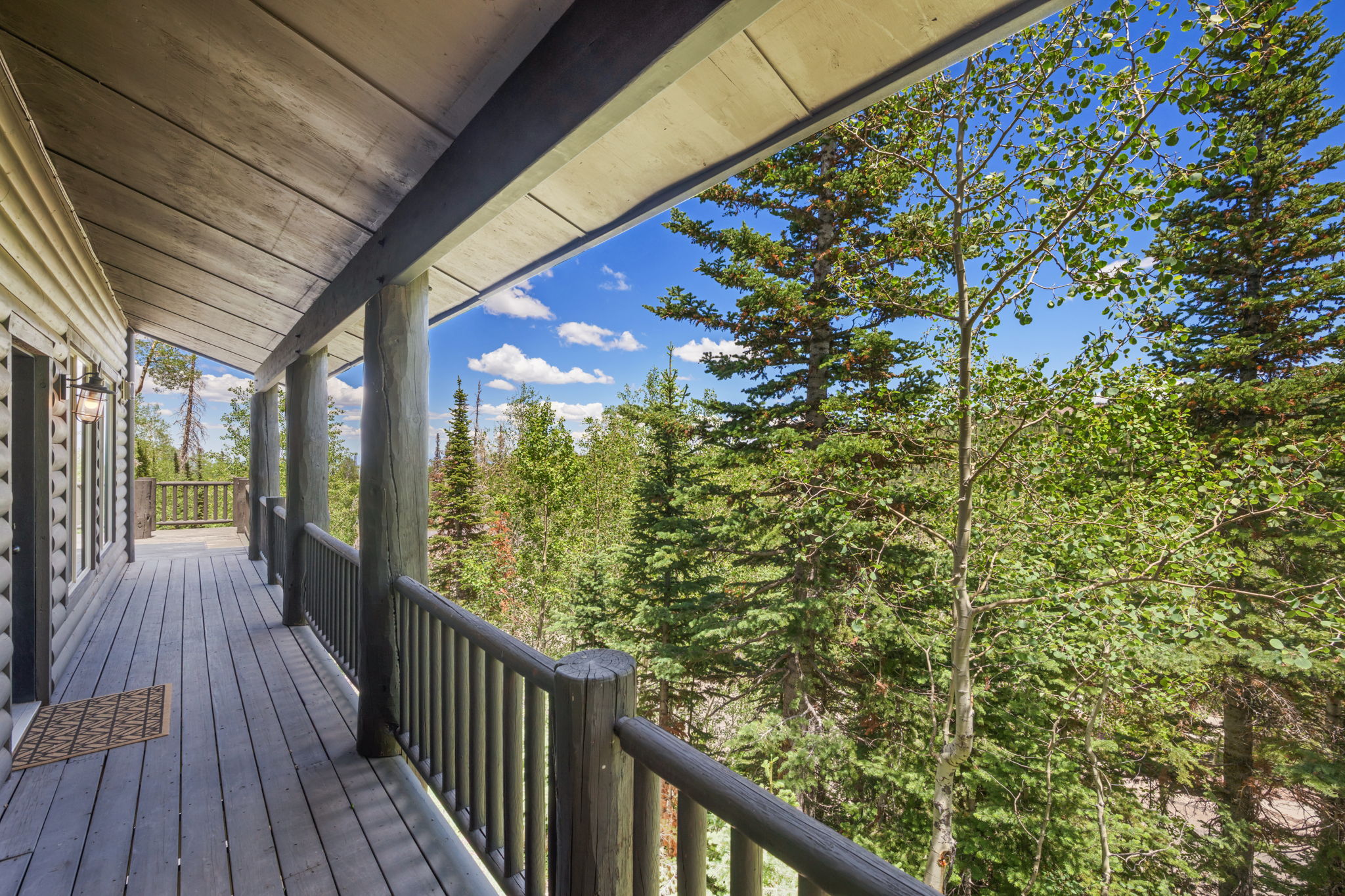 Spacious covered deck with log-style columns and railing, featuring wood decking and a wood-paneled ceiling