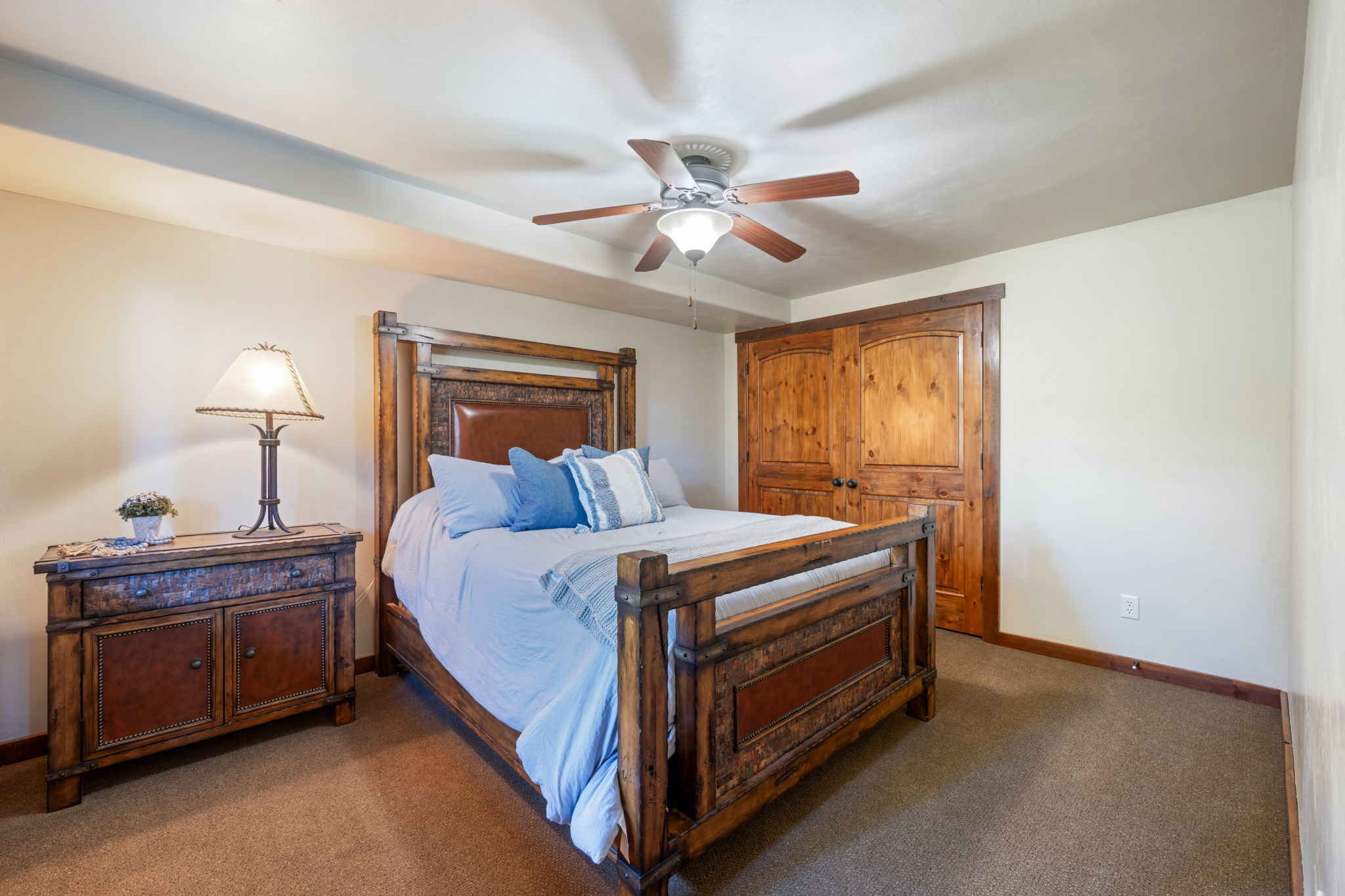 Bedroom featuring rich wood-finish bi-fold closet doors, a ceiling fan with integrated lighting, and neutral tone carpeting