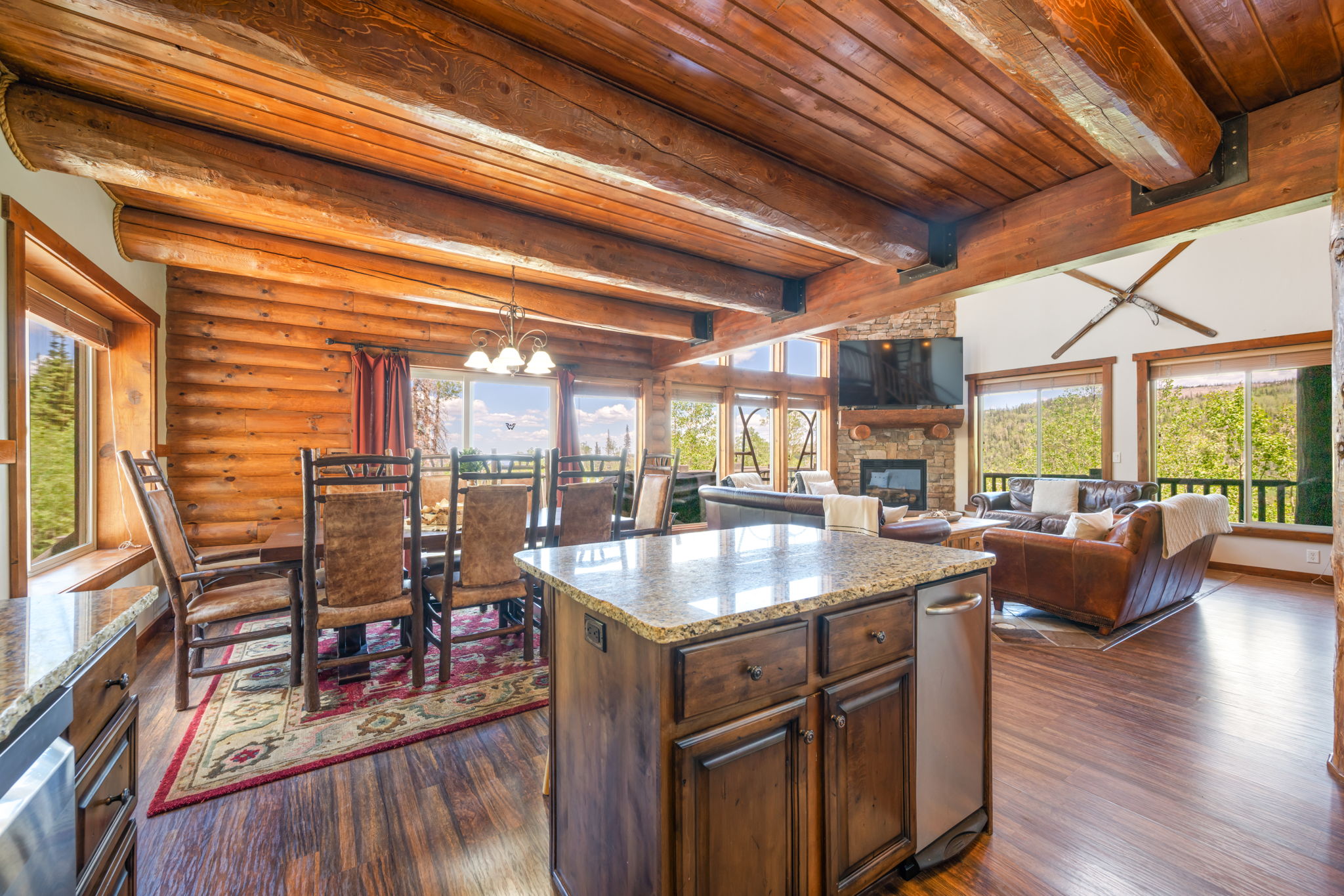 Open-concept living area featuring exposed wood beams, log wall construction, and wood-finish flooring