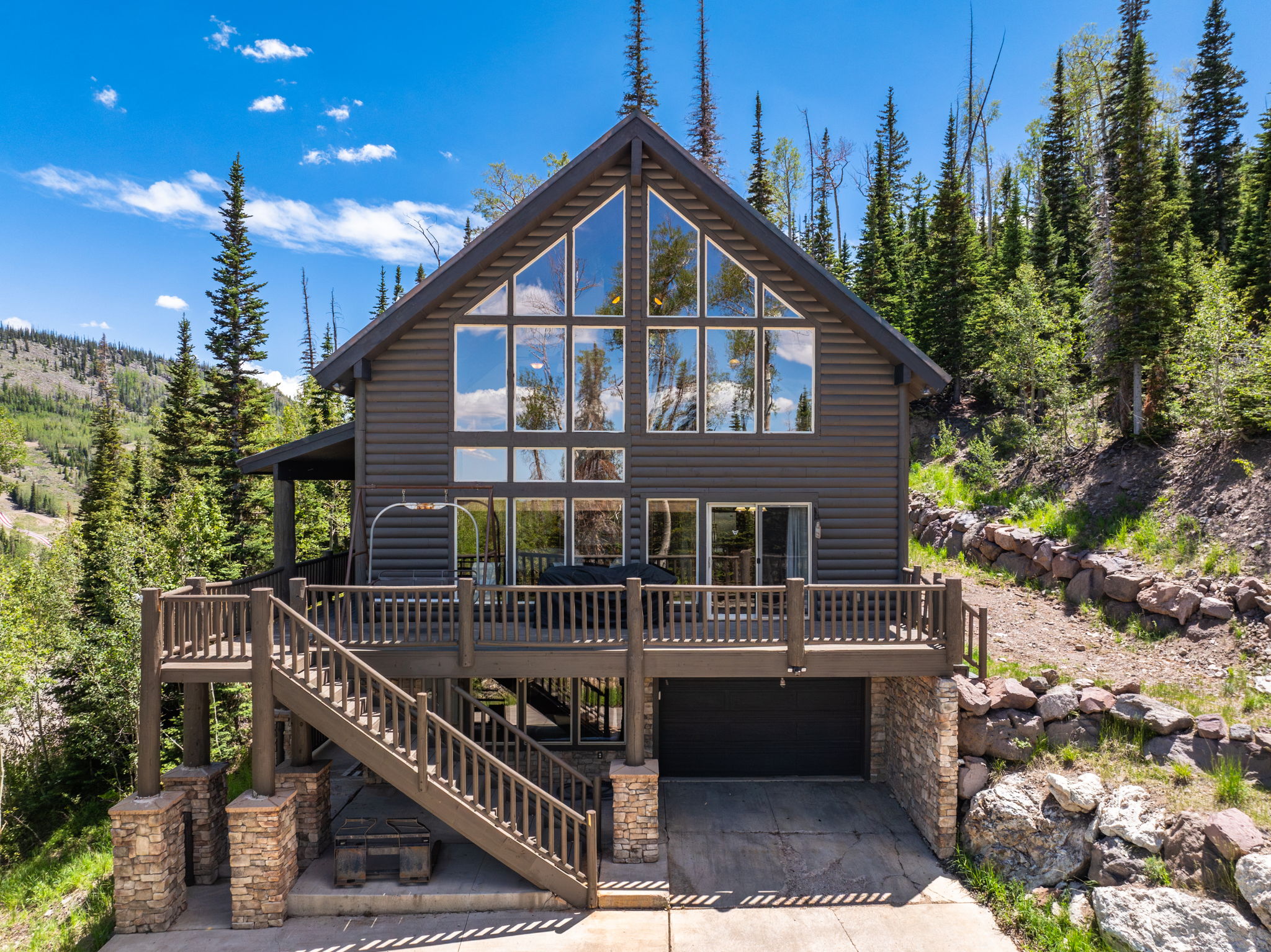 Gable-front home featuring extensive window walls, log siding, and a multi-level deck