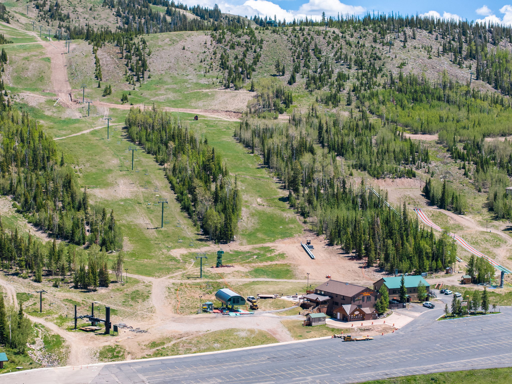 Mountain landscape featuring a ski resort with multiple chairlifts, ski slopes, dense evergreen forests, and a large lodge building