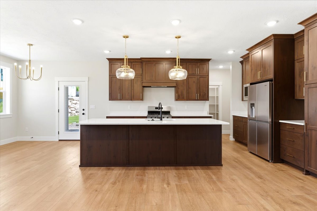 Expansive kitchen featuring a large central island, warm wood-finish cabinetry, stainless steel appliances, and contemporary pendant lighting,