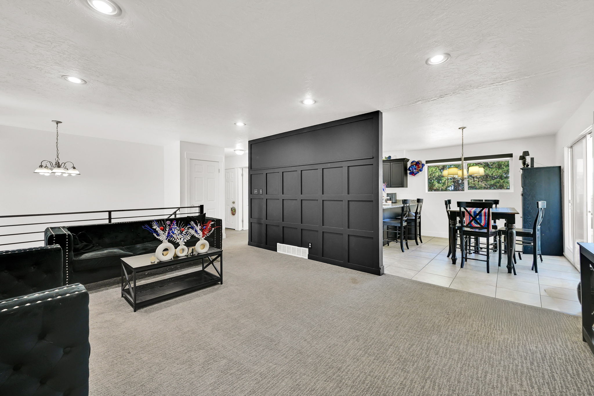Spacious living area featuring light-toned carpet, a black panel accent wall, and recessed lighting
