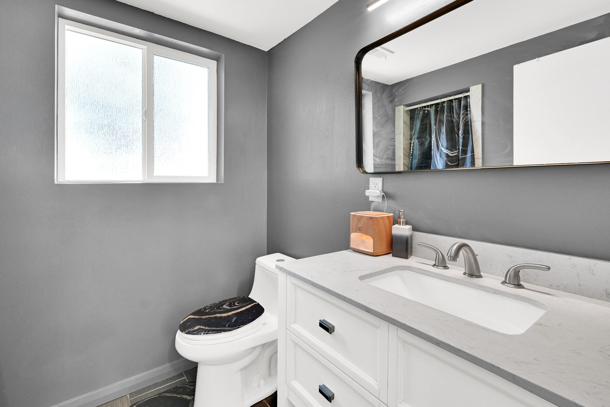 Bathroom featuring a vanity with a white rectangular sink and brushed nickel faucet, a framed mirror, and a frosted window