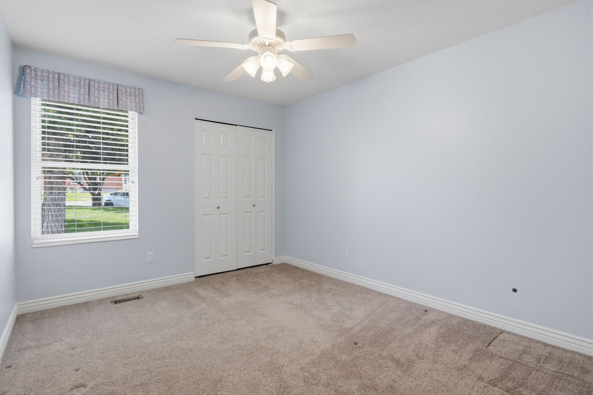 Carpeted room featuring light blue walls, white bi-fold closet doors, and a window with horizontal blinds