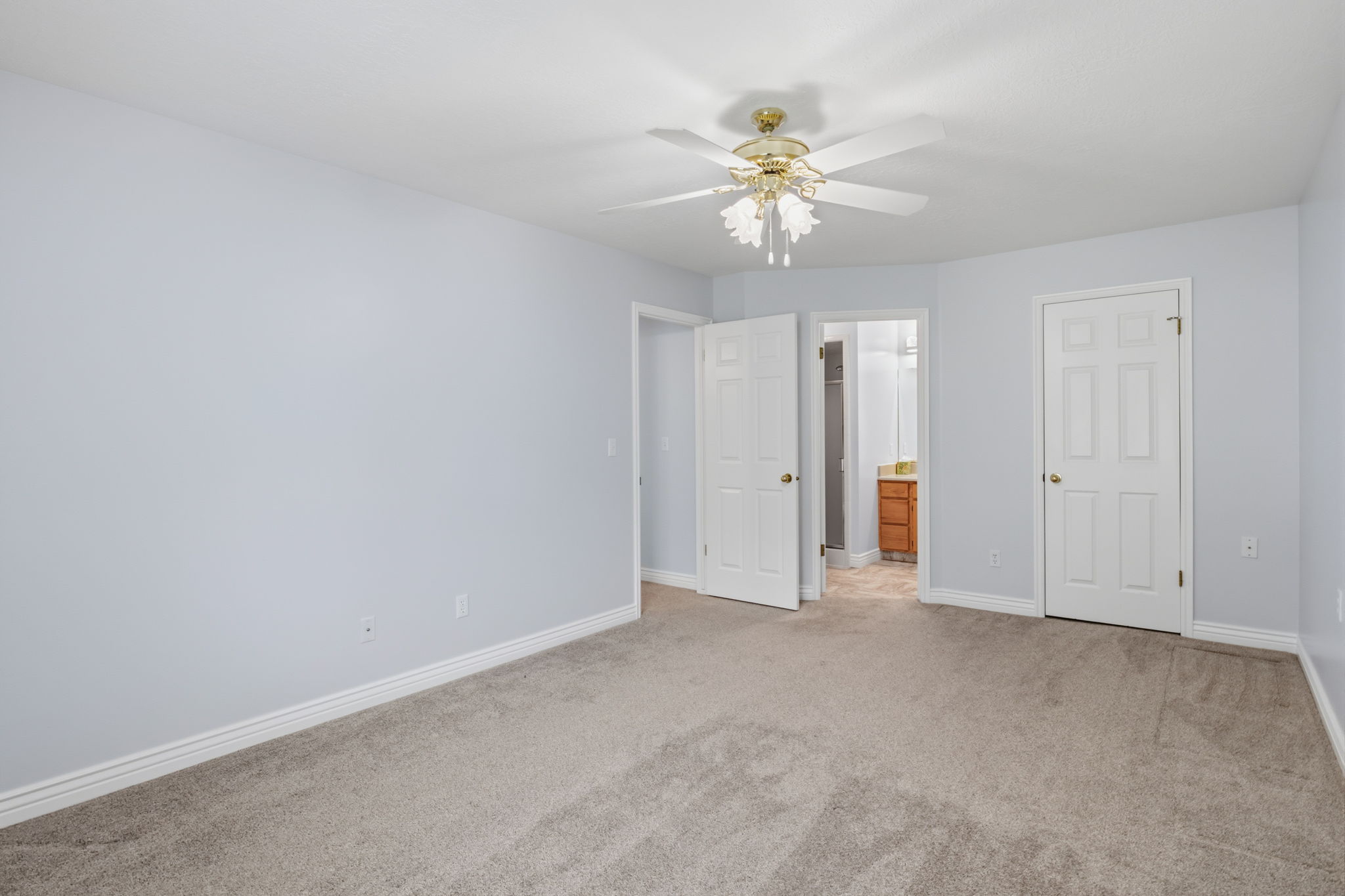 Spacious room featuring light gray wall paint, carpeting, white baseboards, and a ceiling fan with integrated lighting