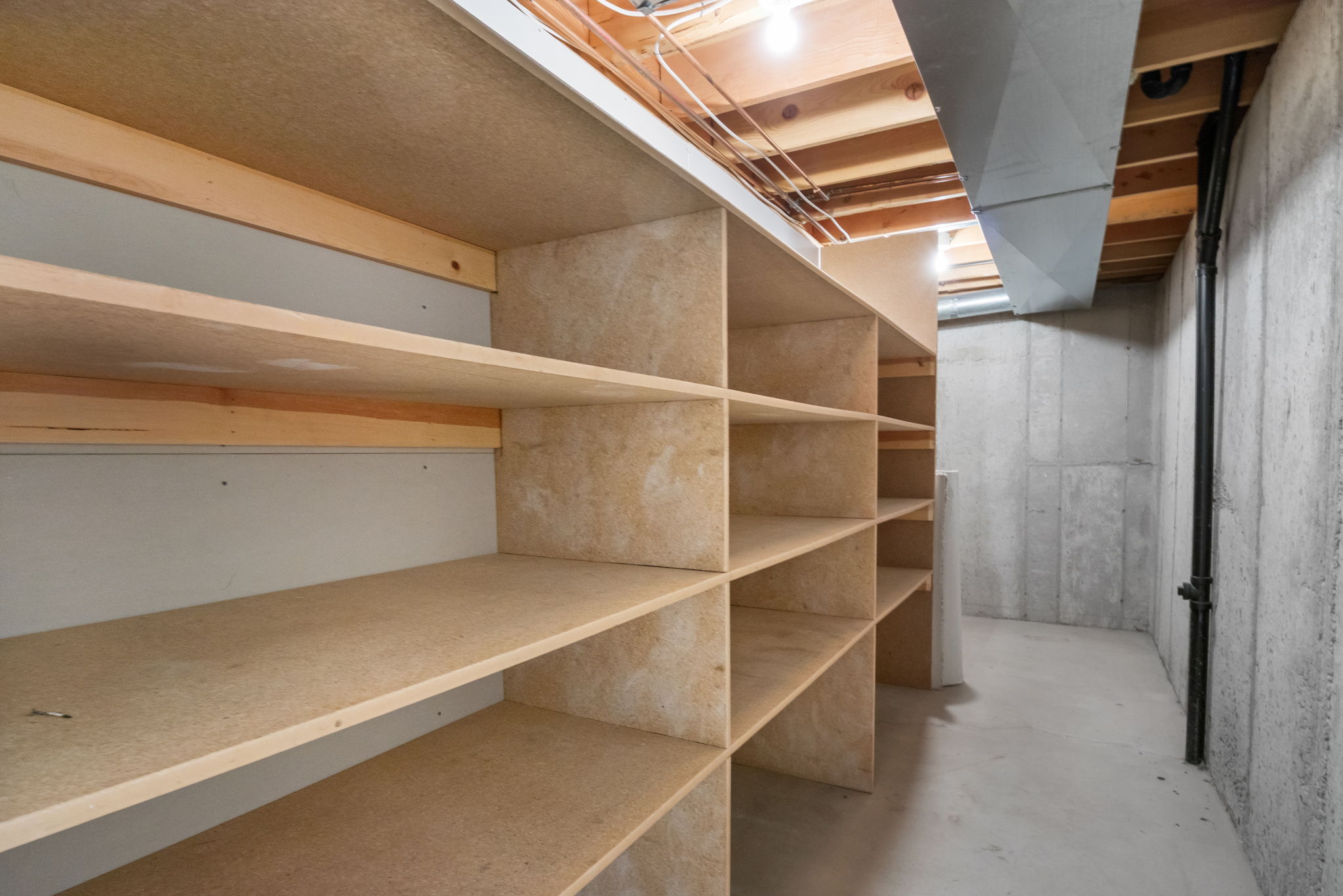 Built-in open shelving providing extensive storage, concrete flooring, exposed ceiling joists, and visible utility conduits