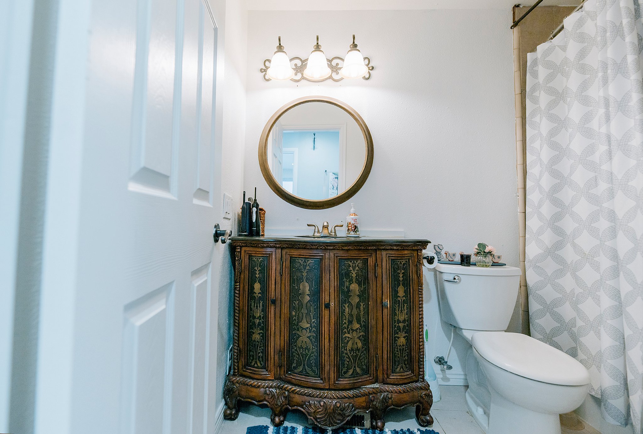 Bathroom featuring an ornate wood vanity with a stone countertop, a round framed mirror, and a three-light fixture