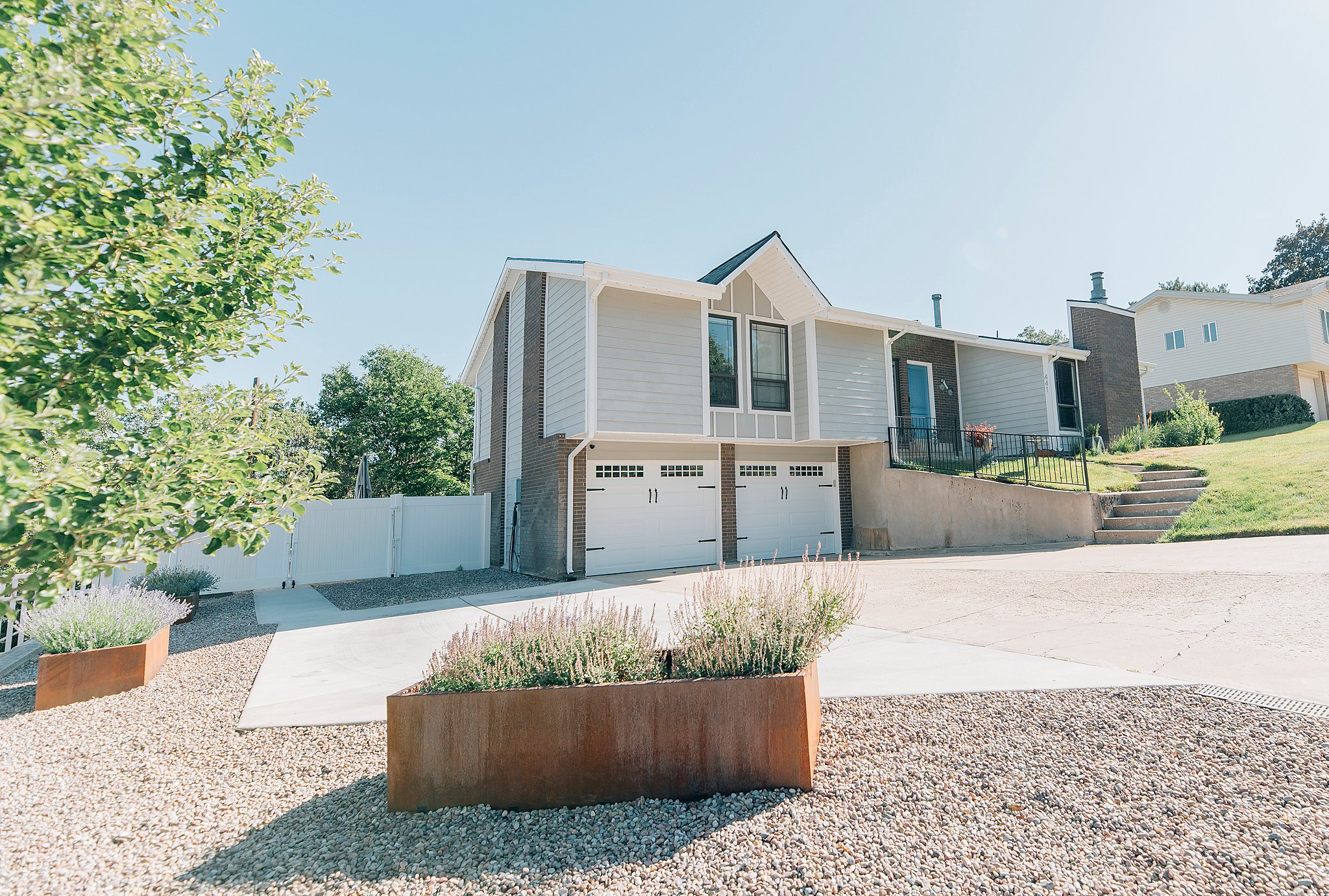 Split-level residence featuring light gray siding, a two-car garage with white paneled doors, black window trim, and a concrete driveway