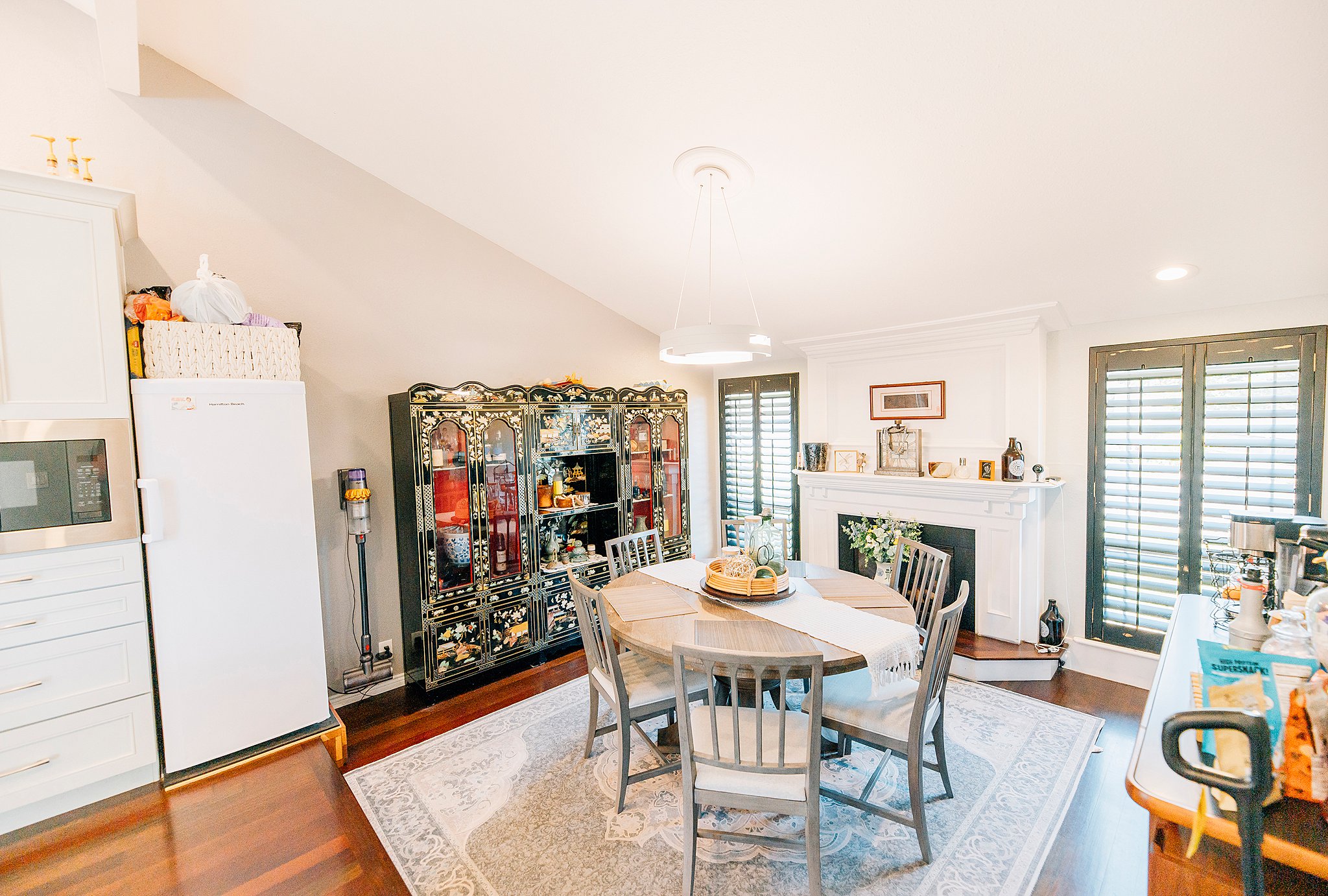 Open-concept living space featuring a fireplace with a detailed mantel, dark wood plantation shutters, and rich wood-finish flooring