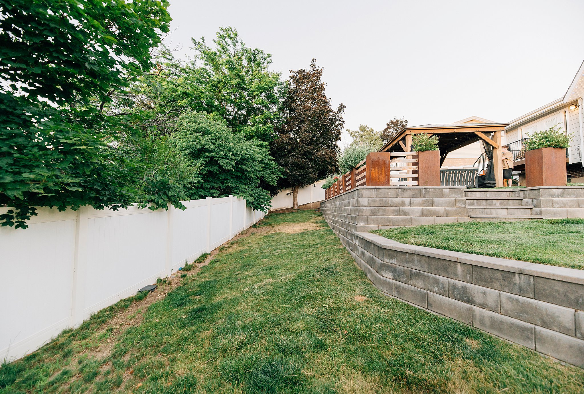 Tiered backyard with retaining walls, a white vinyl privacy fence, and mature perimeter trees