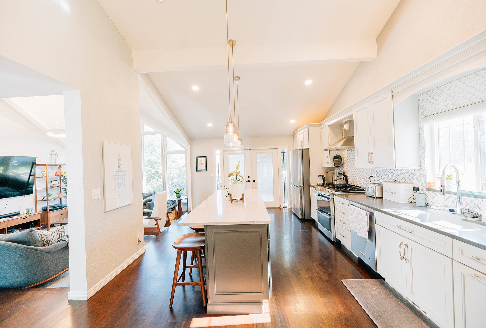 Modern kitchen featuring vaulted ceilings, wood-finish flooring, white cabinetry, a large kitchen island with a light-toned countertop, and stainless steel appliances