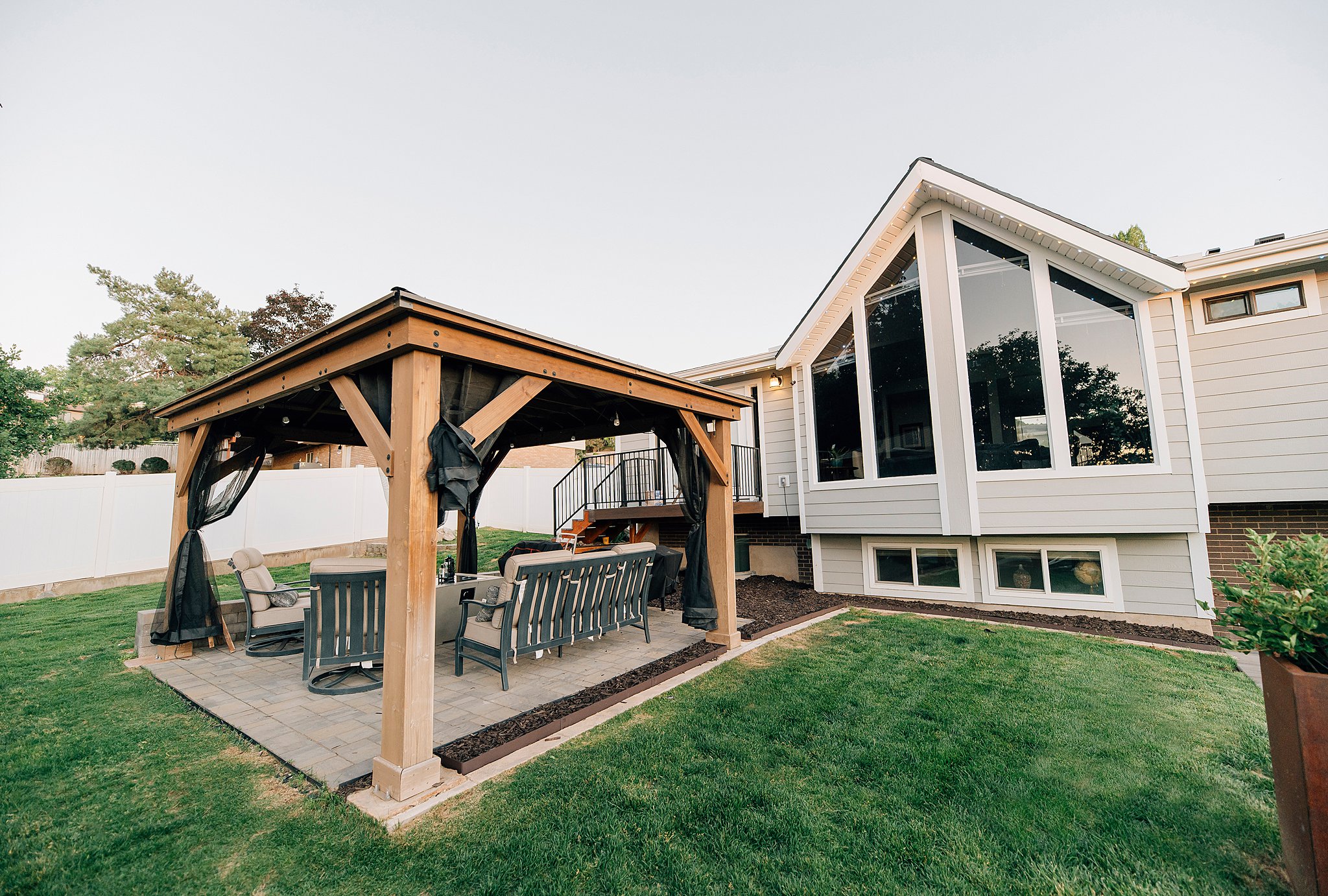 Expansive backyard featuring a manicured lawn, a wood-frame gazebo with a paved patio, and a multi-level deck with black railings