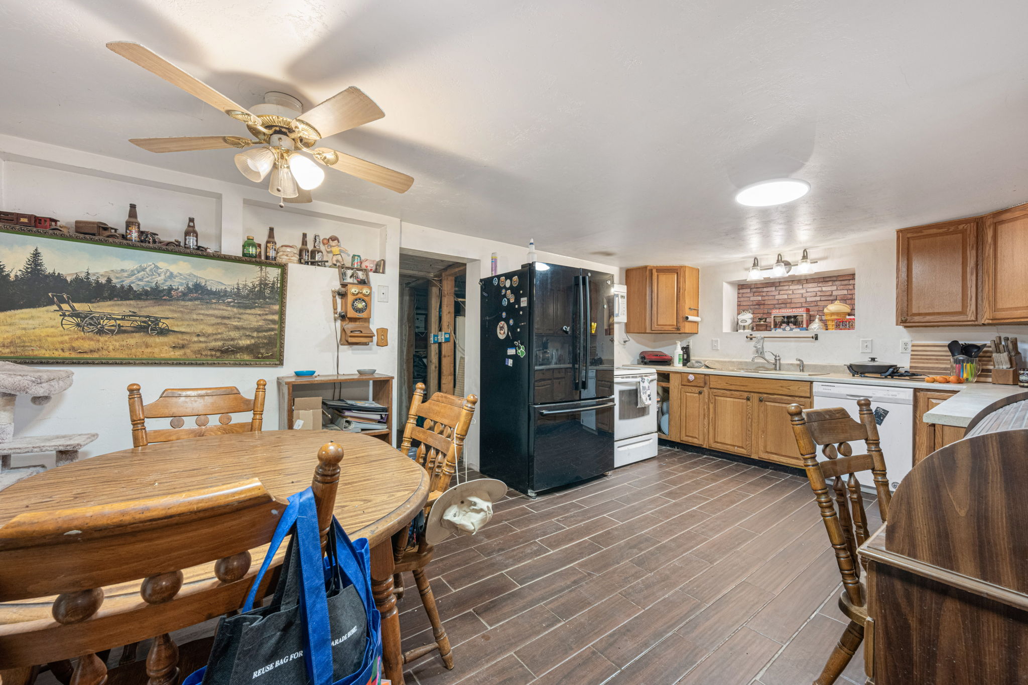 Spacious kitchen and dining area featuring wood-finish flooring, a ceiling fan, light wood cabinetry, a built-in kitchen sink, and a black French door refrigerator