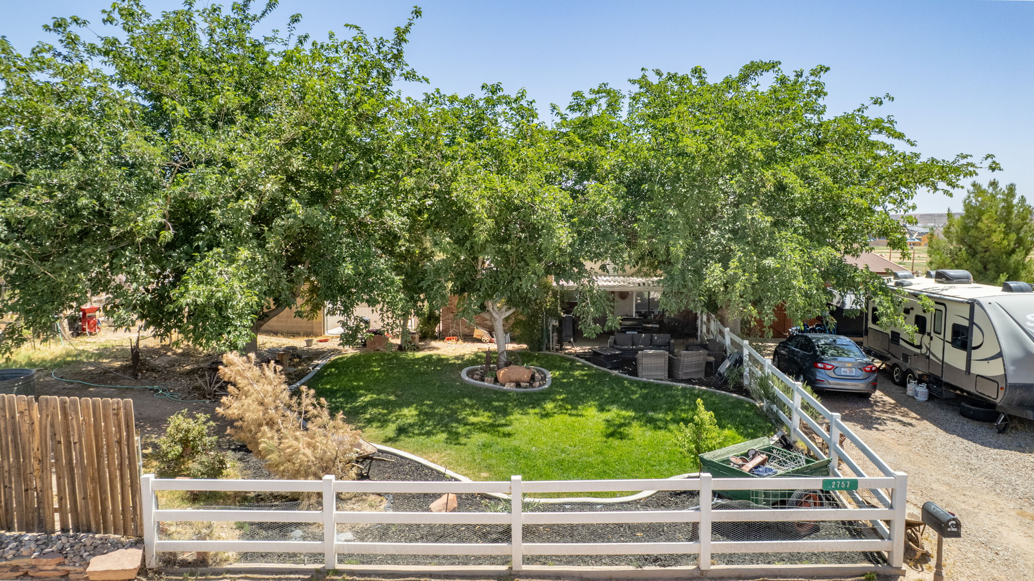 Front yard featuring a white picket fence, a manicured lawn, mature shade trees, and decorative rock landscaping