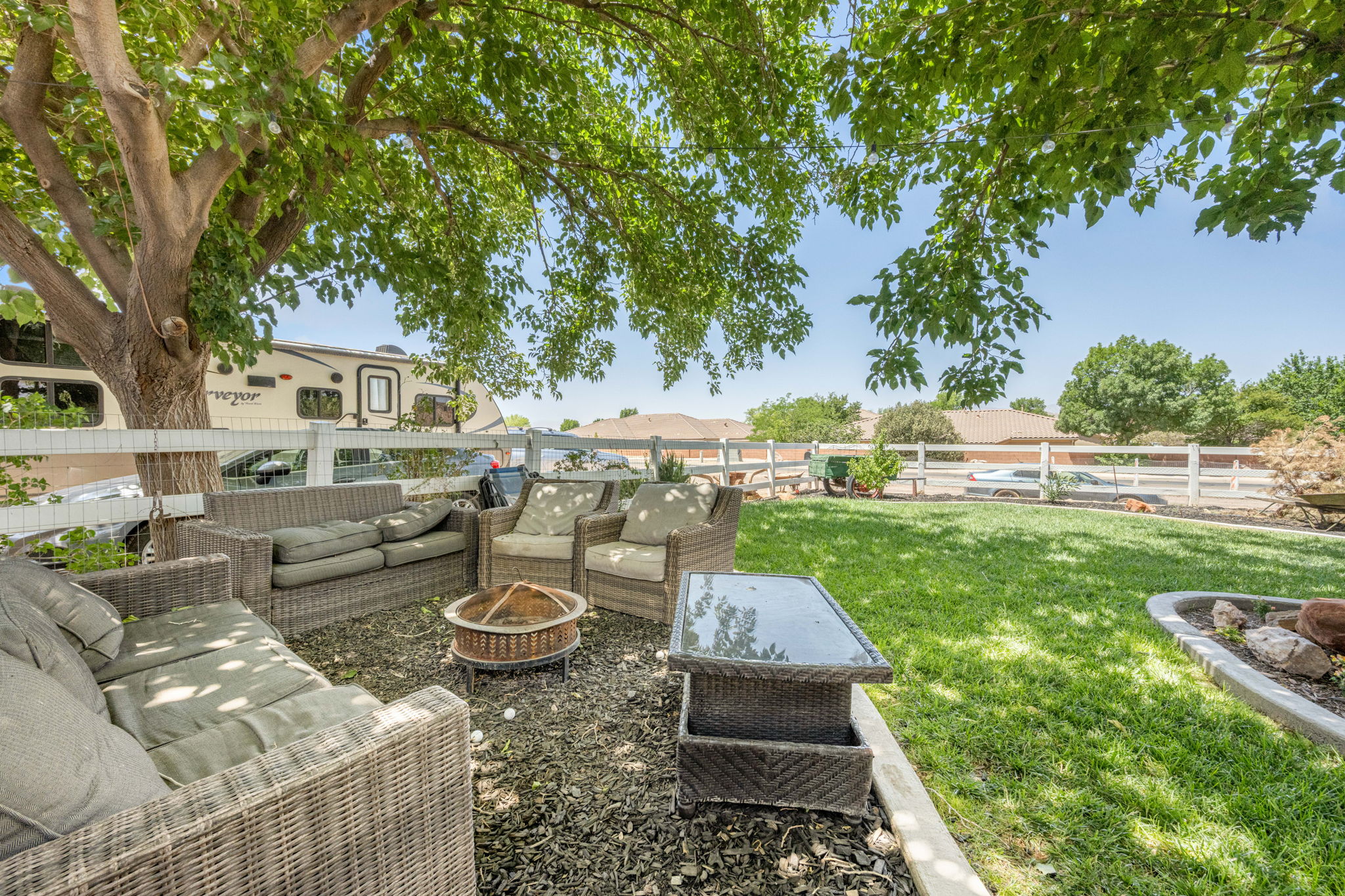 Expansive backyard featuring a manicured lawn, a large shade tree, a decorative white fence, and a defined gravel patio area