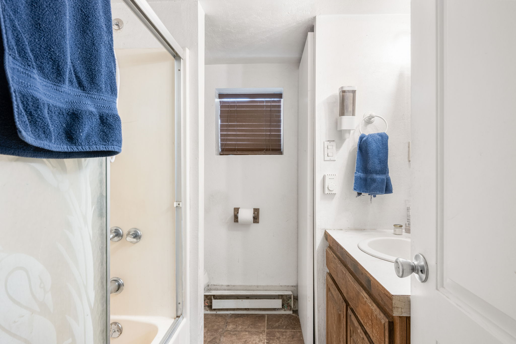 Bathroom featuring a shower-over-tub combination with sliding glass doors, a vanity with a white countertop and integrated sink, wood-finish cabinetry, and a window with horizontal blinds