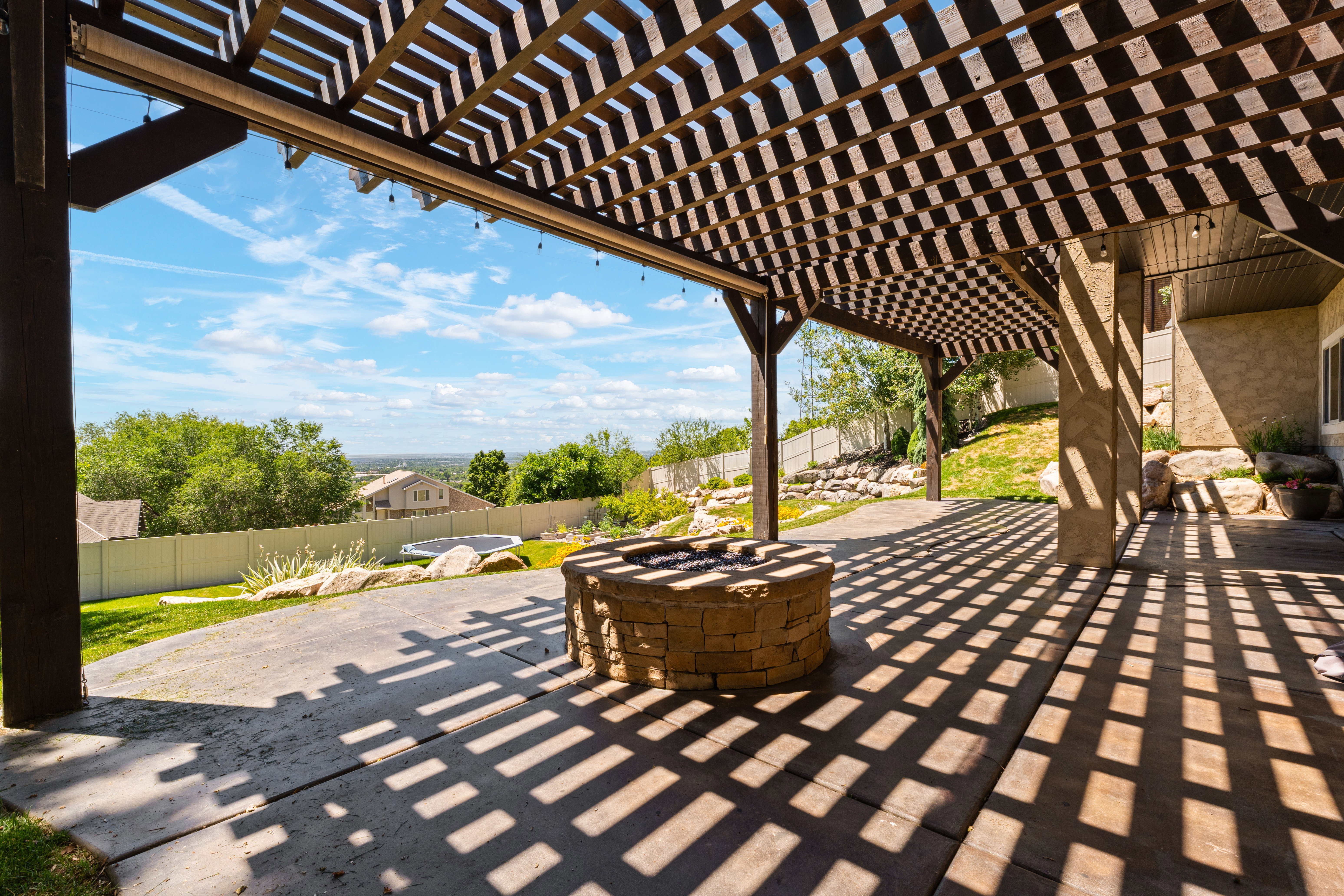 Covered patio featuring an open-slat pergola, a built-in stone fire pit, and a concrete patio surface
