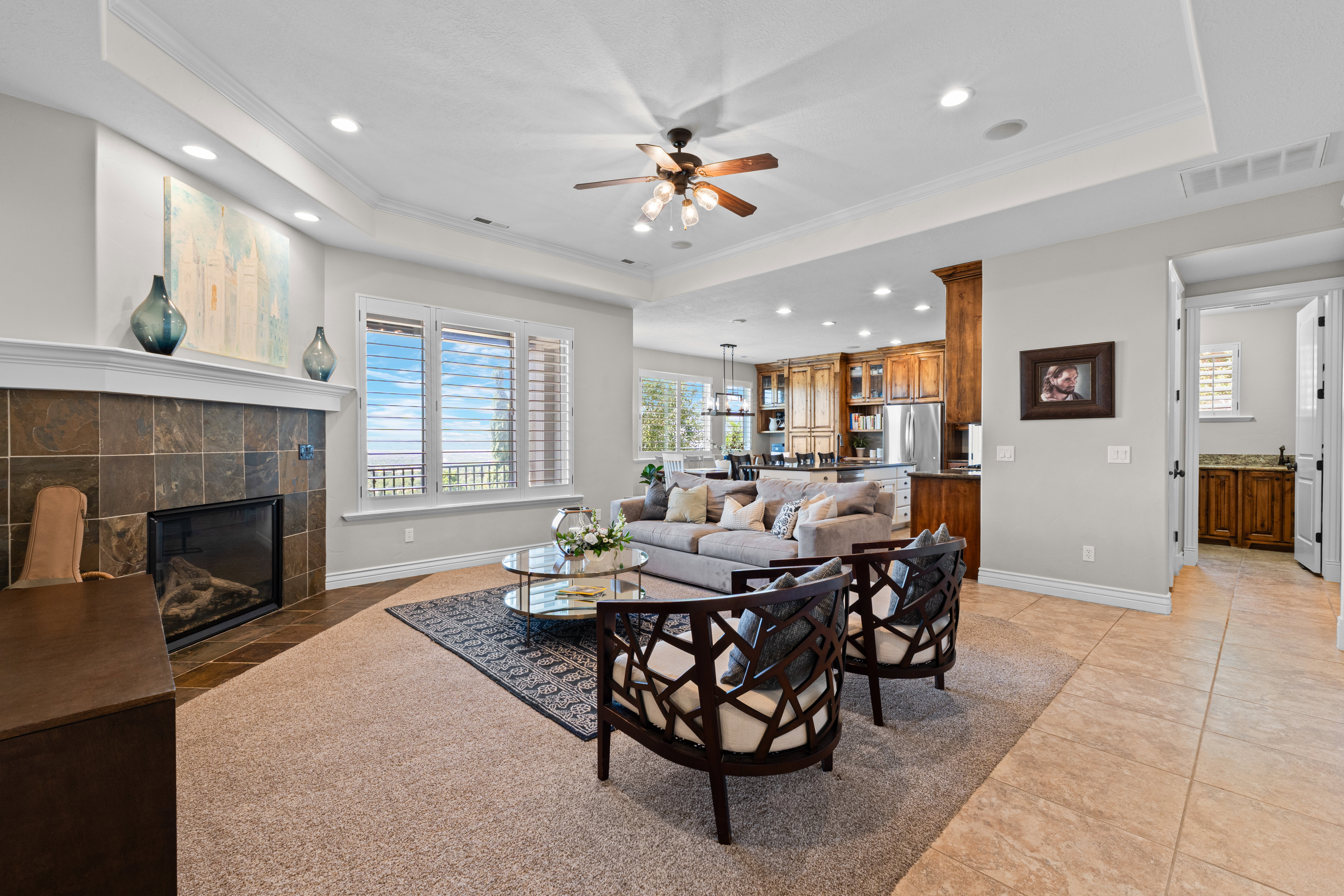 Spacious living area featuring a tile-surround fireplace, coffered ceilings with recessed lighting, and large windows with horizontal blinds