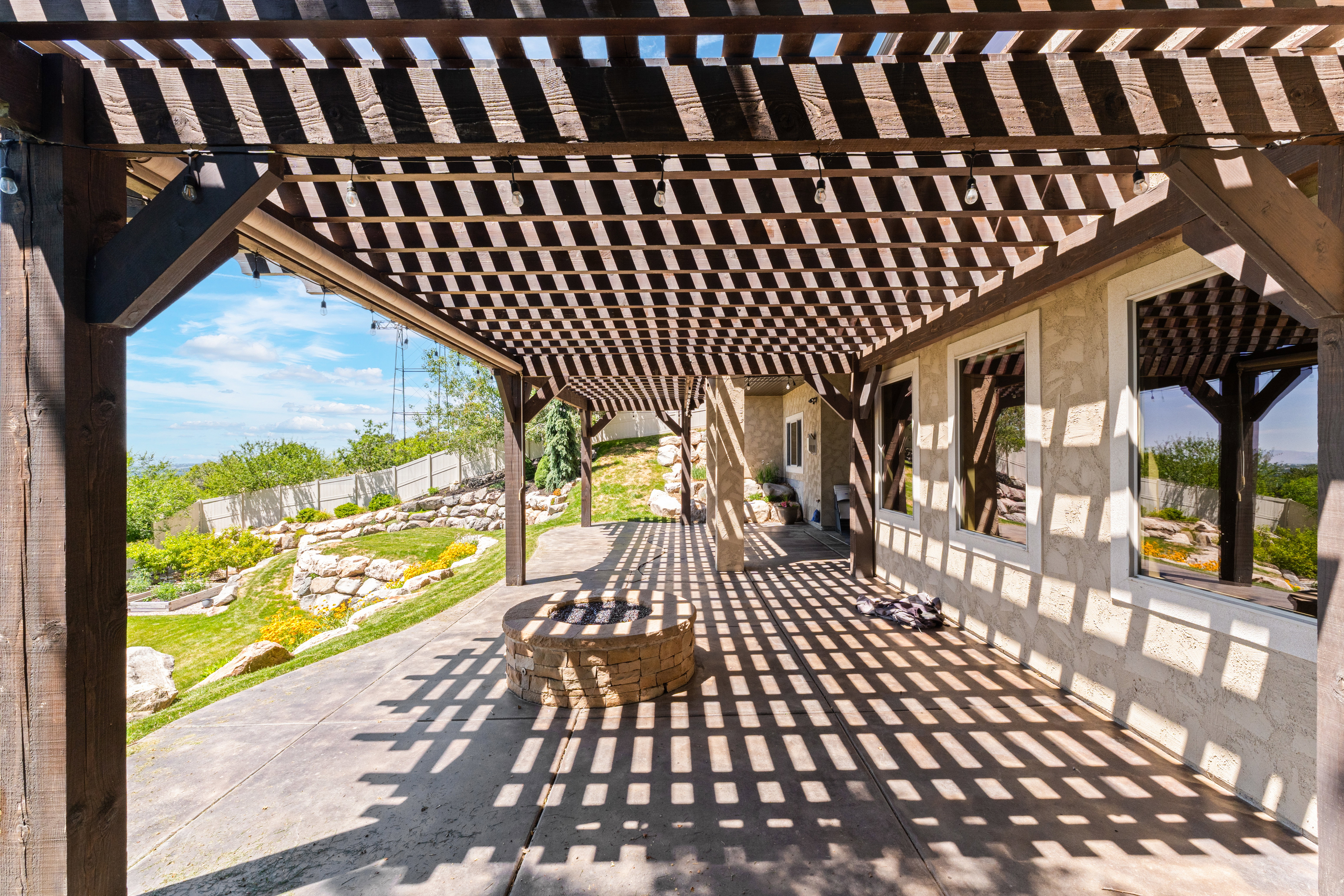 Expansive patio featuring a wooden pergola, stone fire pit, concrete flooring, and multiple windows