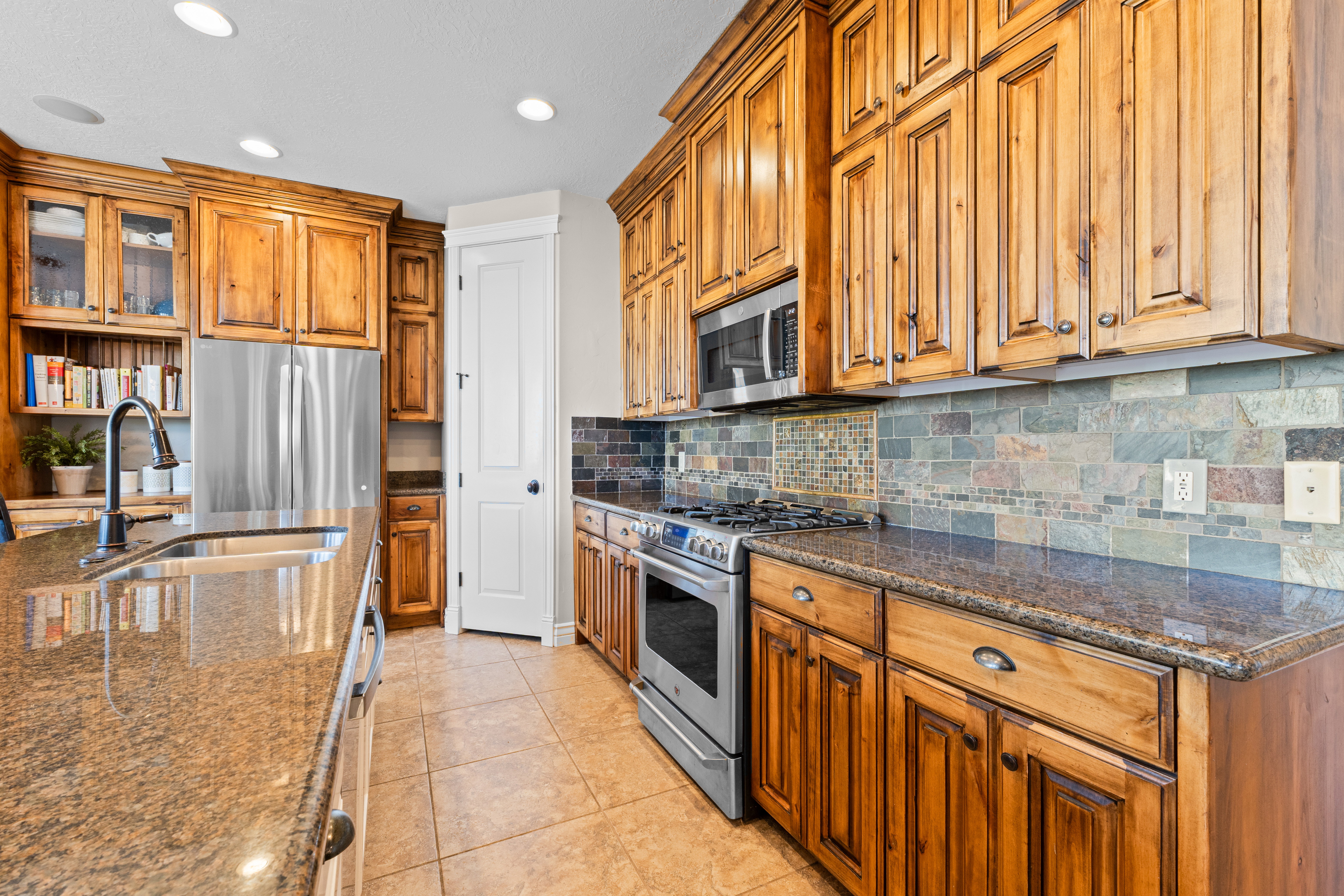 Kitchen featuring natural wood cabinetry with crown molding, stone countertops, a tile backsplash, stainless steel appliances, and recessed lighting