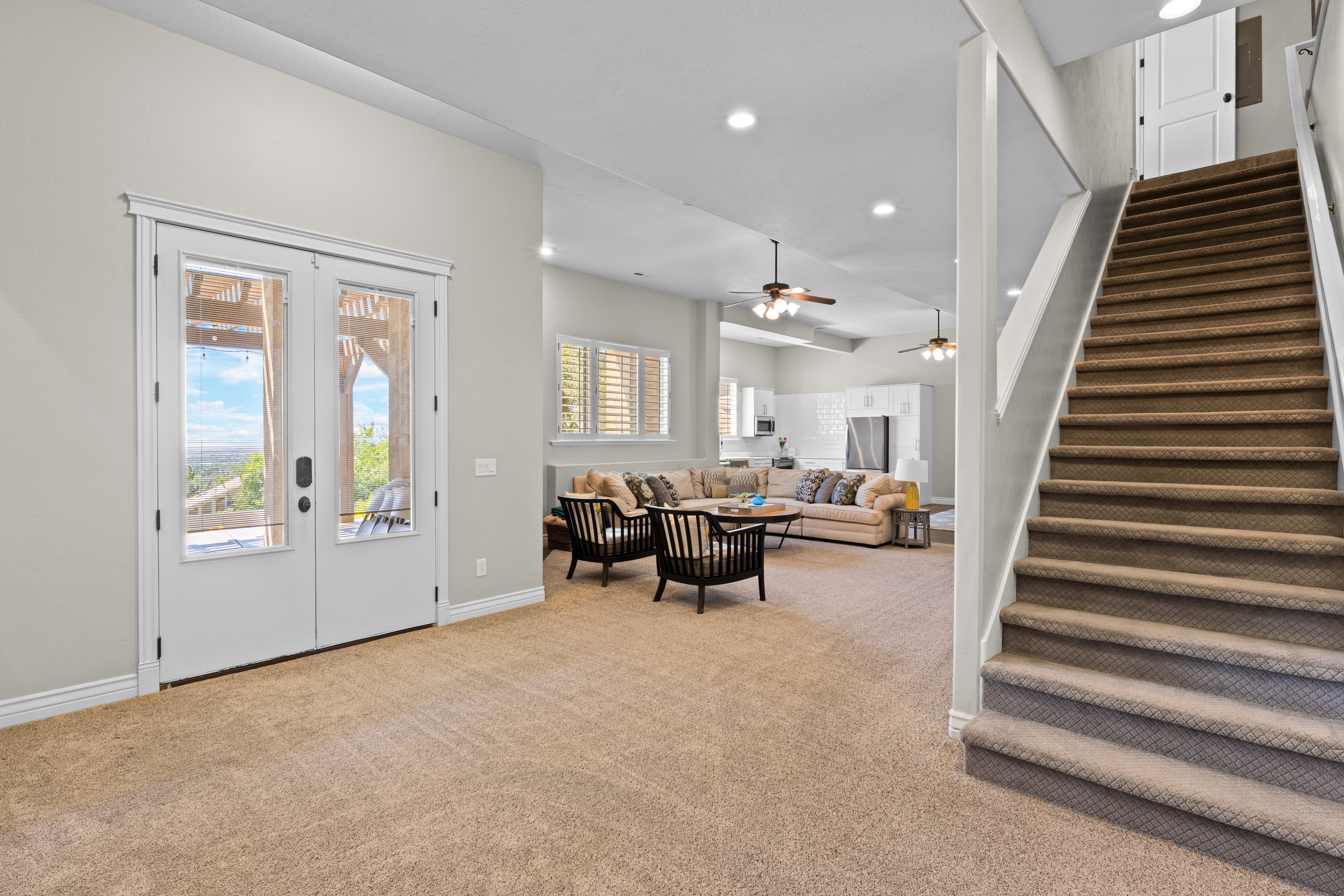 Spacious open-concept lower level featuring neutral carpeting, white trim, and a white staircase with a contrasting gray handrail