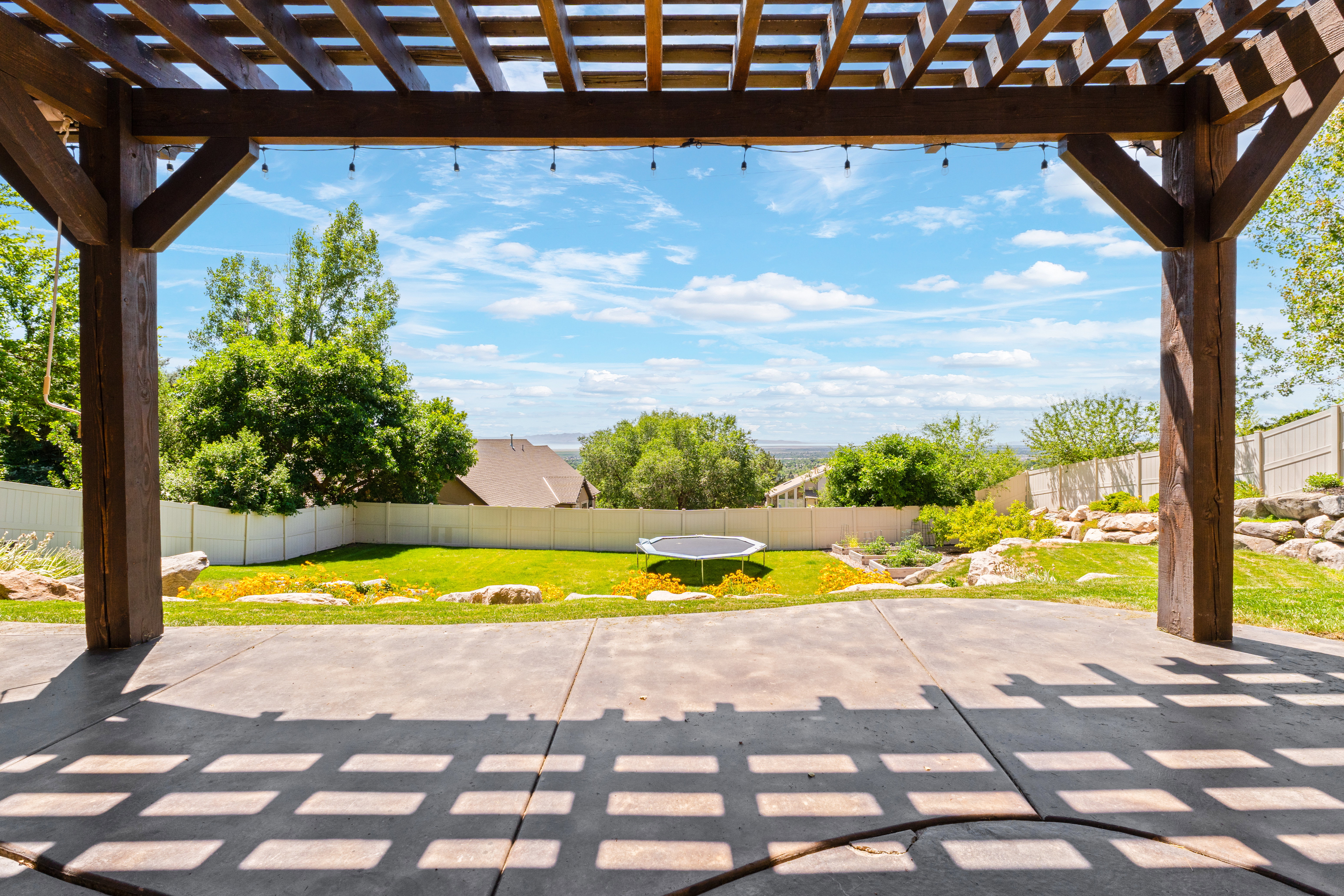 Expansive patio with a wood pergola structure, string lighting, and direct access to a tiered backyard