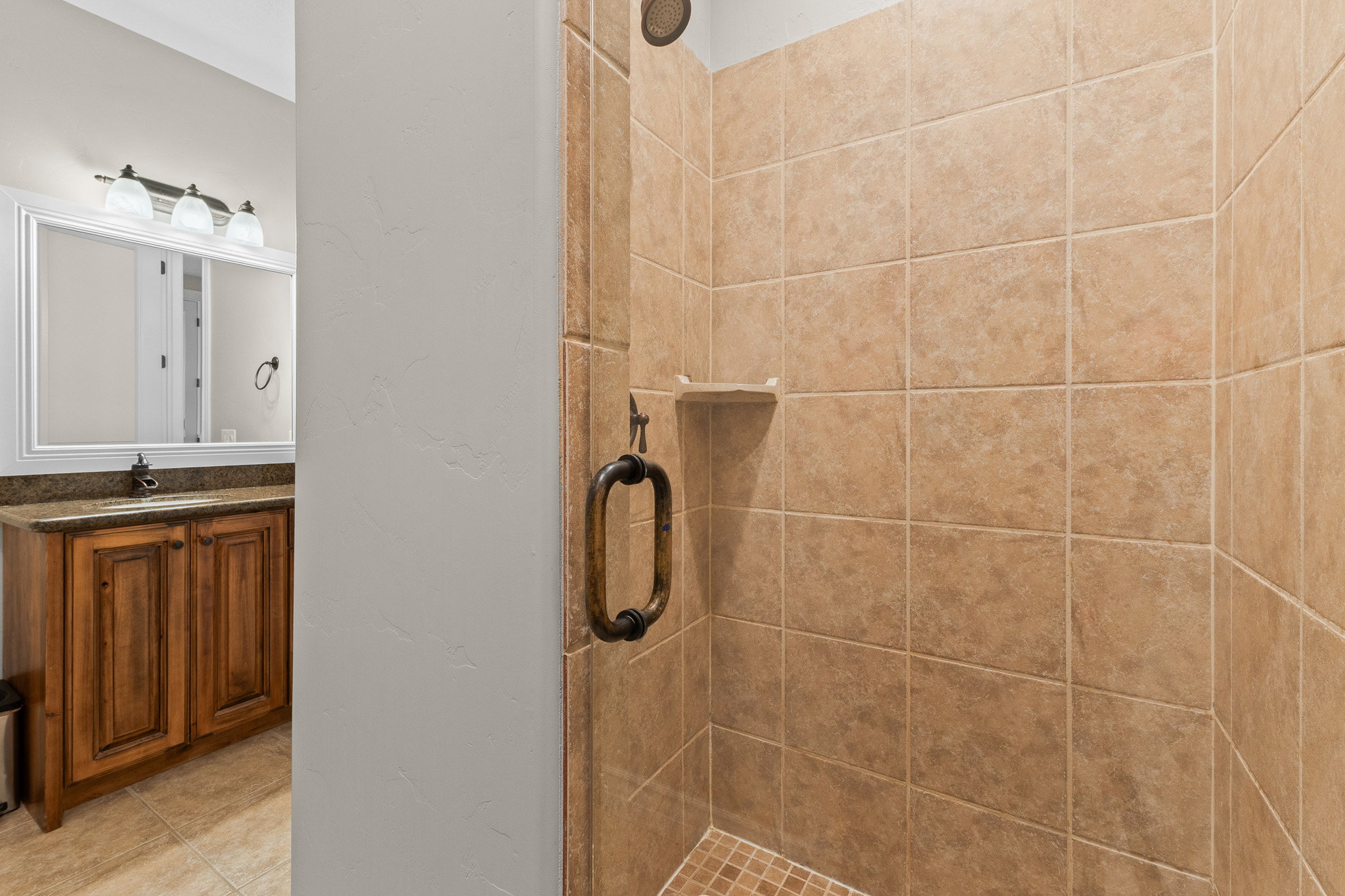 Walk-in shower featuring ceramic tile surround, recessed shelf, and bronze hardware