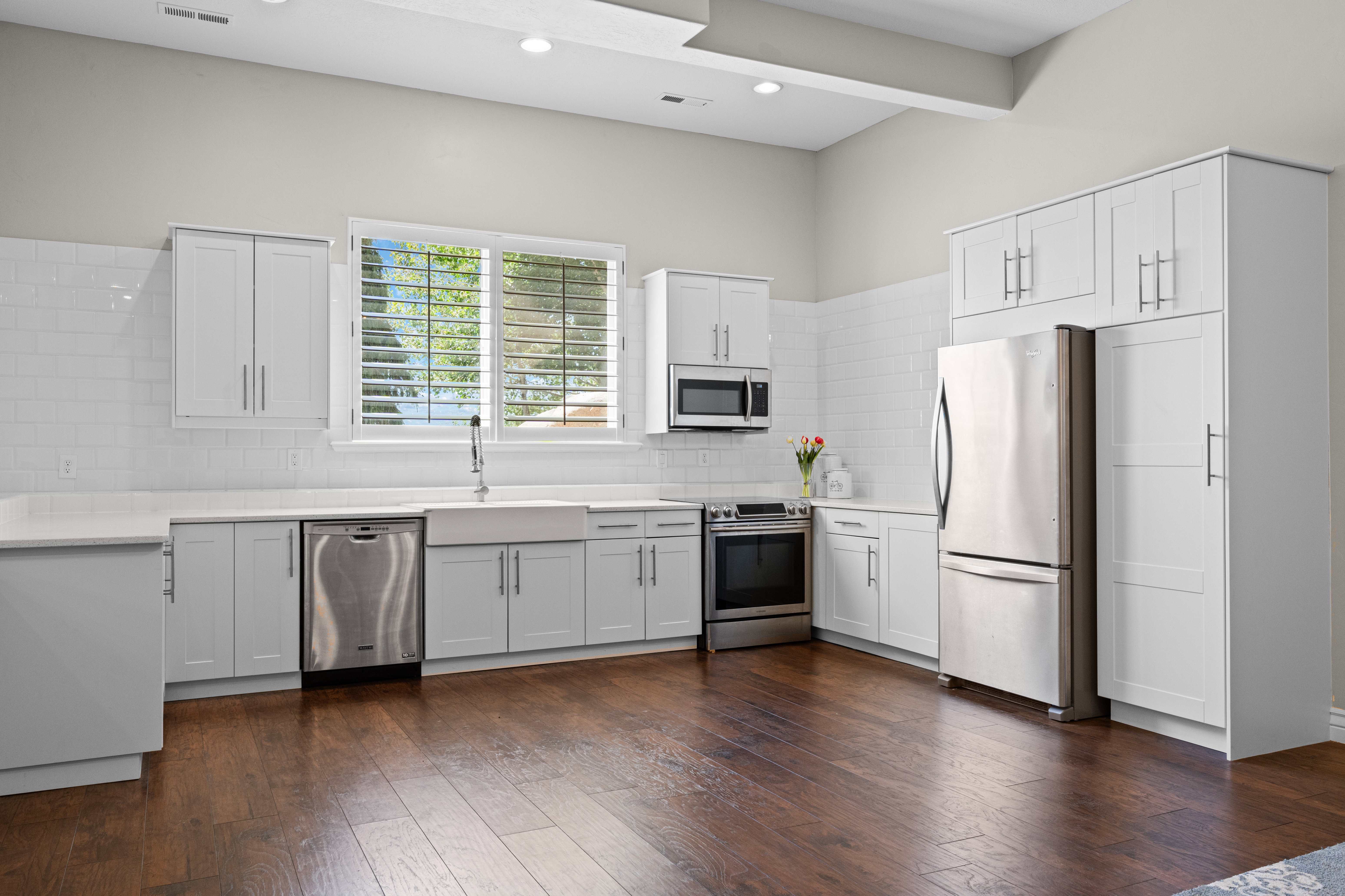 Contemporary kitchen featuring wood-finish flooring, white shaker cabinetry, stainless steel appliances, a farmhouse sink, and white subway tile backsplash